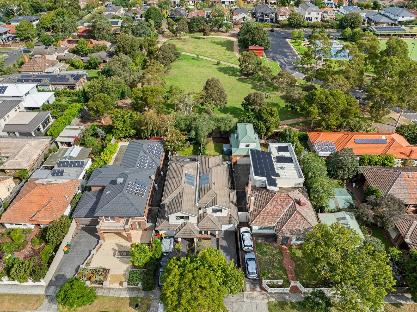 An aerial view of Ormond, Melbourne neighborhood showing houses with solar panels on roofs, green trees, a park with a walking path, and sports courts surrounded by trees.