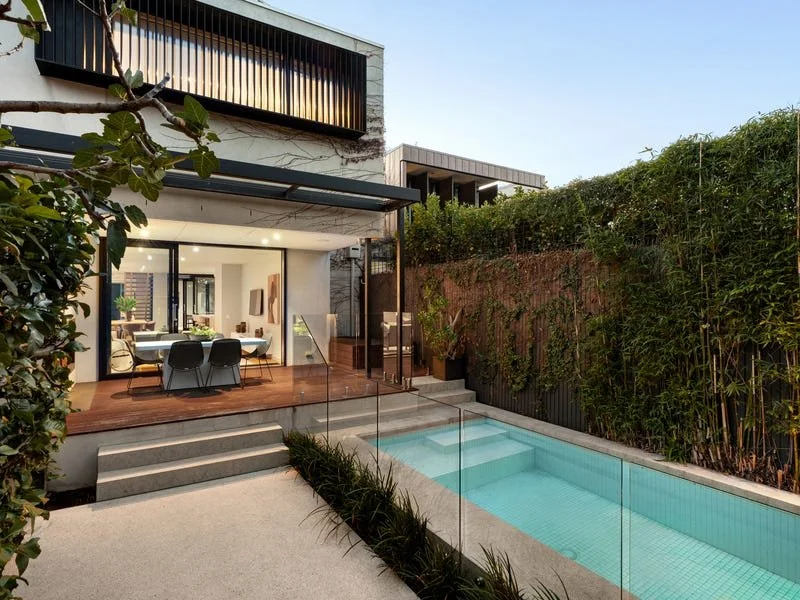 Modern townhouse in Elwood, Melbourne with large glass doors opening to a backyard with a pool, surrounded by greenery and a wooden deck.