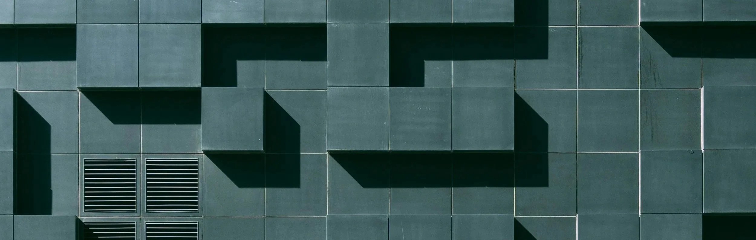 Close-up photo of a modern building's exterior wall with geometric green panels and ventilation grates.