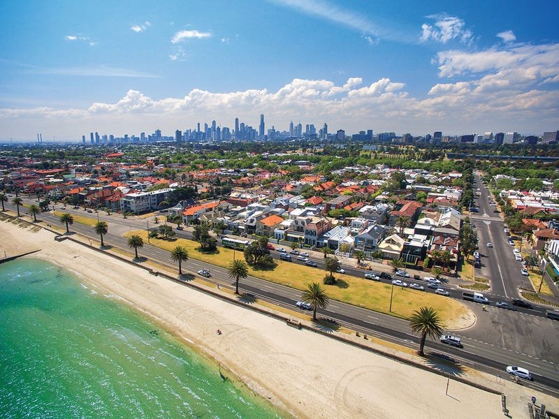 An aerial shot of the beach at Albert Park looking back over the suburb and homes, with the city in the background