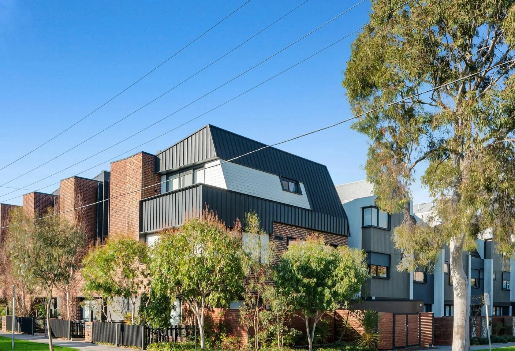 Modern multi-story residential building in McKinnon, Melbourne, with brick and metal siding, surrounded by trees and a clear blue sky.