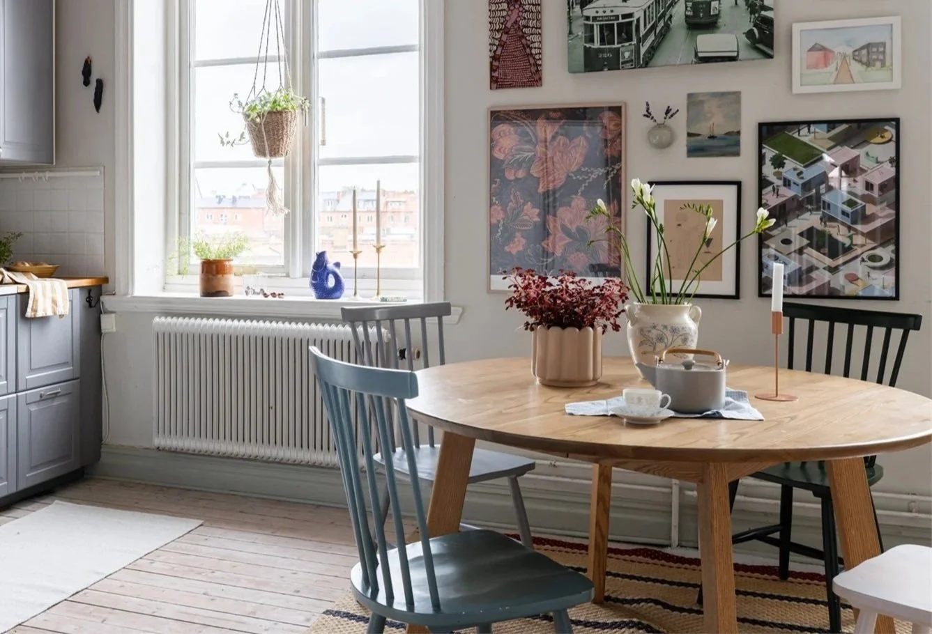 Ett matbord med fyra stolar, dekorerat med vaser och ljusstakar, samt ett fönster med utsikt över ett bostadsområde, och väggar med konstverk.