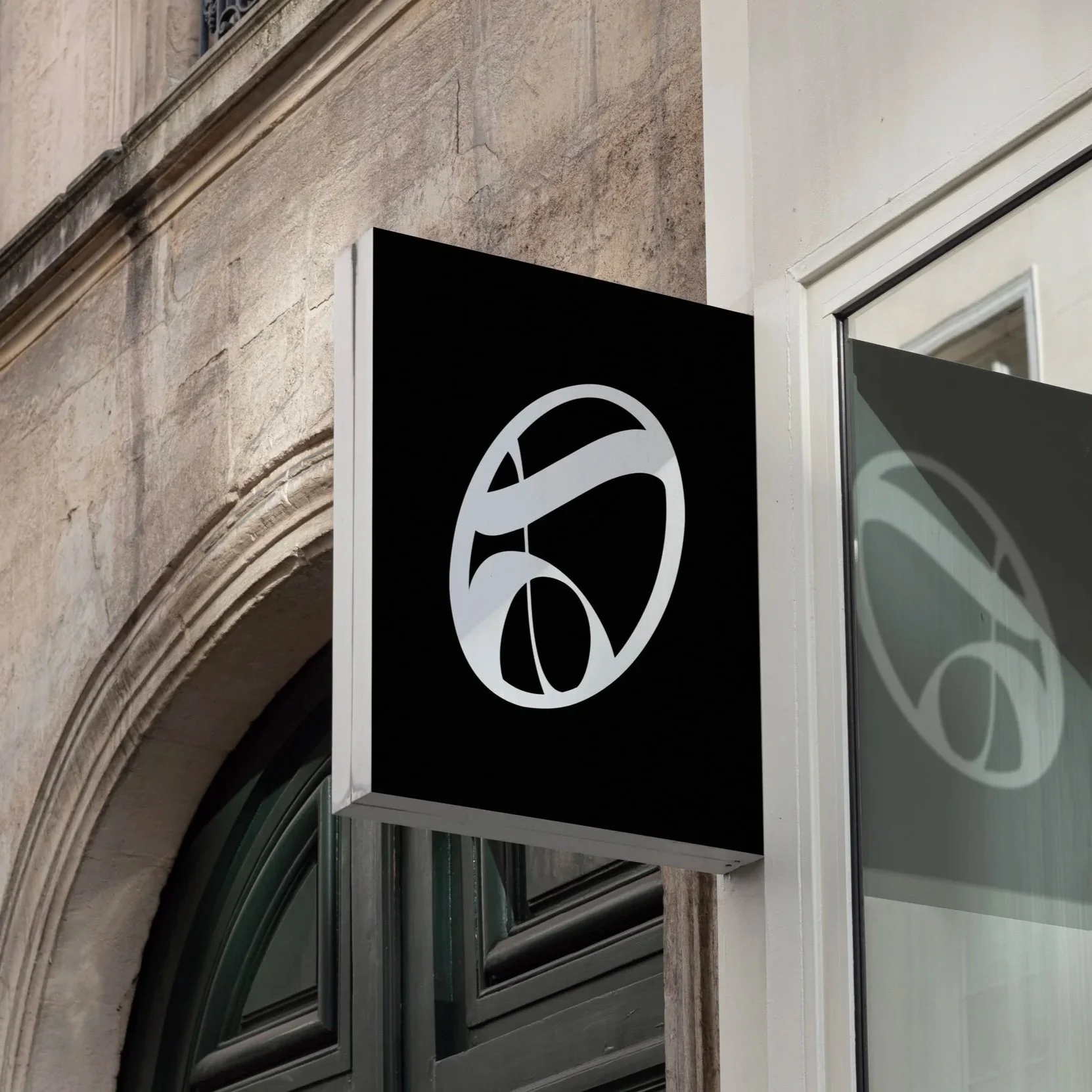 Black square sign with a white abstract logo on the side of a building.