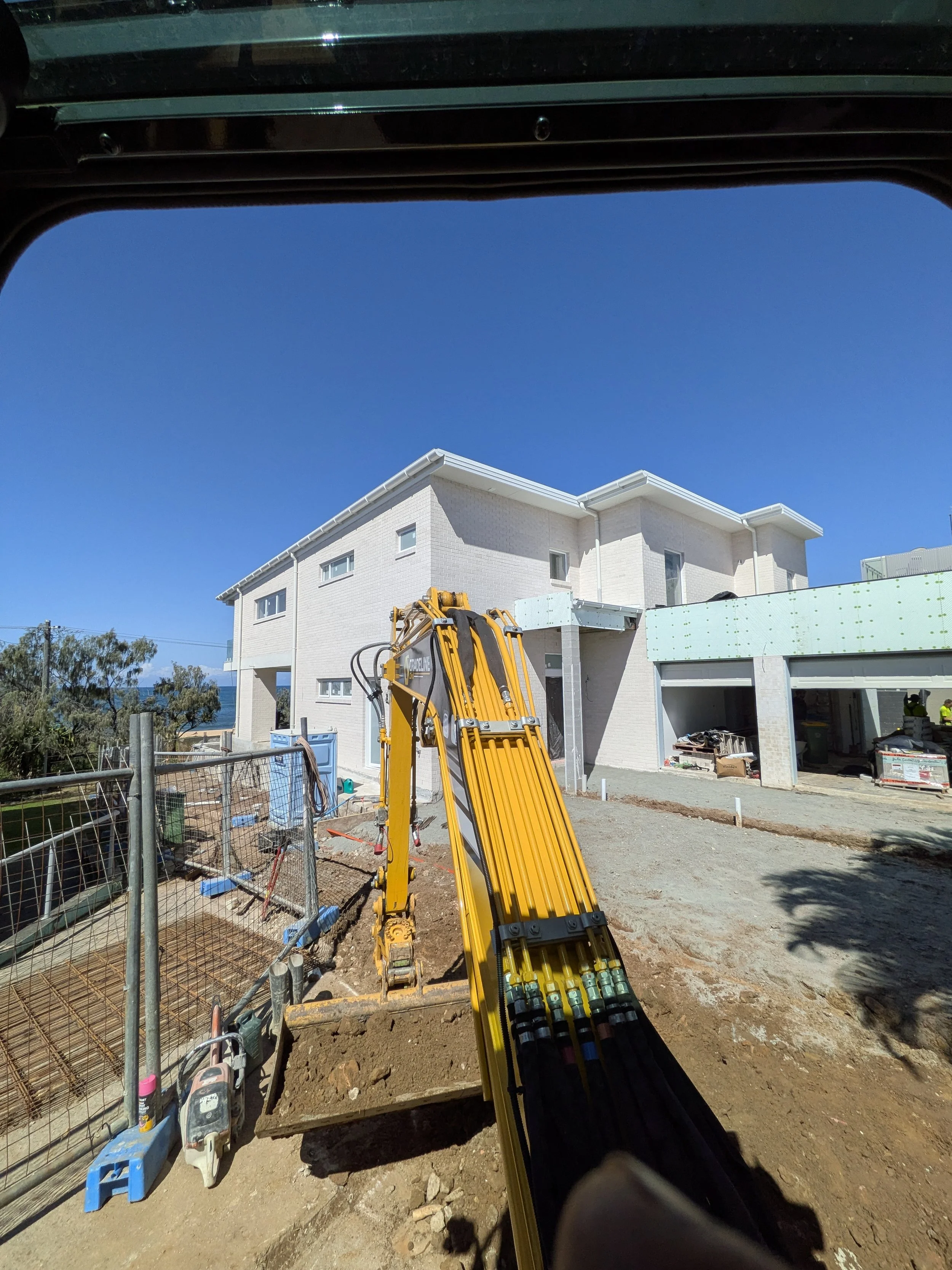 Construction site with a white house, construction equipment, and a yellow hydraulic breaker tool.