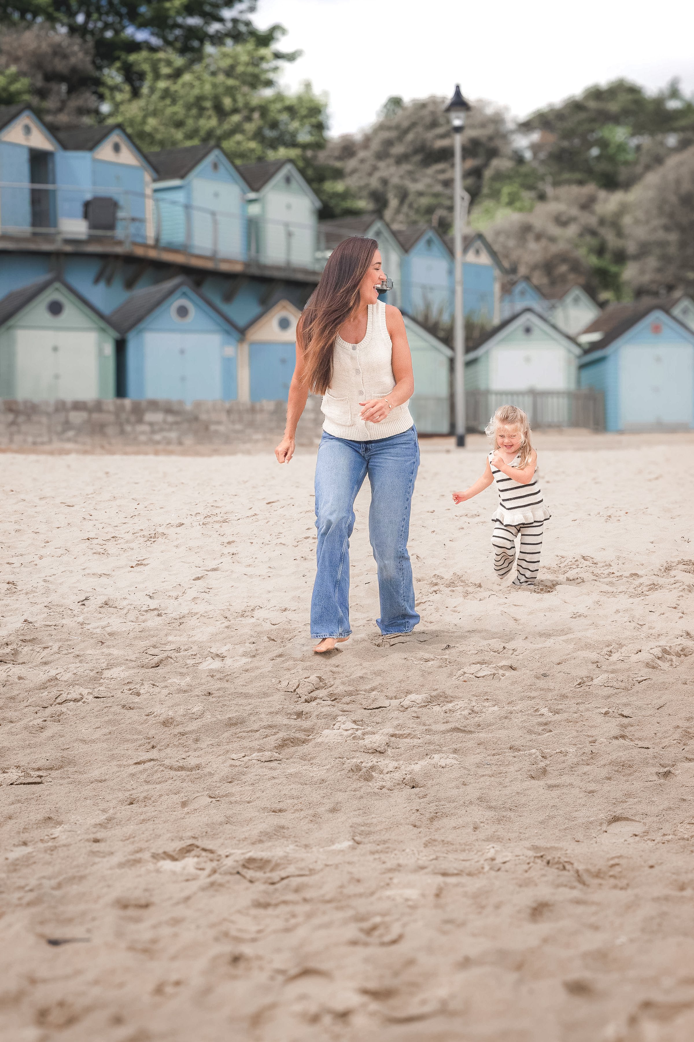 A woman and a child playing on a sandy beach in front of colorful beach huts.