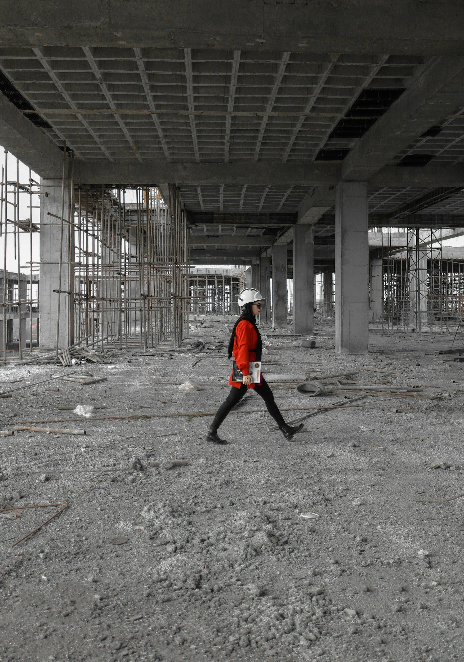 Construction worker walking at a construction site with unfinished concrete and scaffolding.