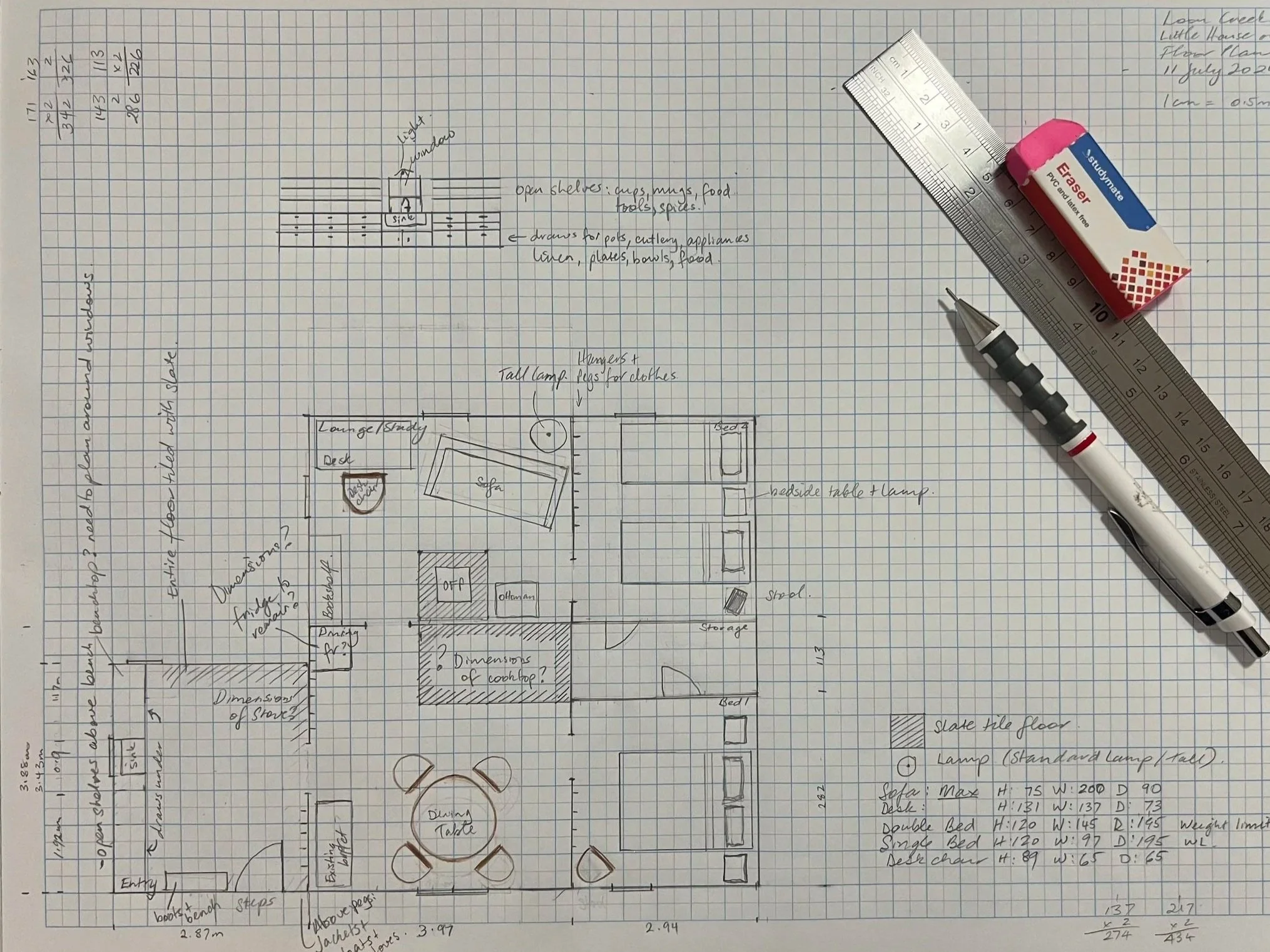 Hand-drawn floor plan of a tiny house on graph paper, depicting various rooms and measurements with notes about furniture and fixtures for kitchen, living area, bedroom, and dining space. Items include sofa, desk, beds, table, storage, and lamps, with annotations about dimensions and materials.