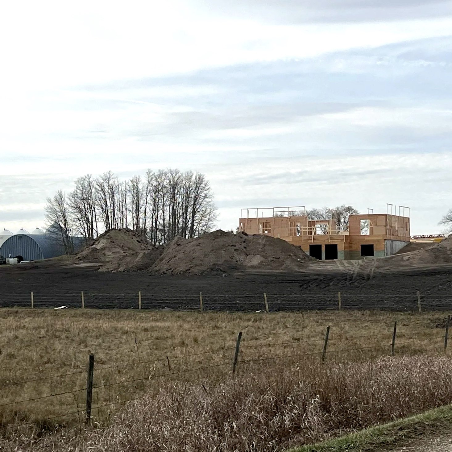 Construction site with wooden framing and open window and door frames, over a flat landscape with a cloudy sky.