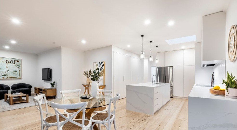 Open-concept kitchen and living room with white walls, light wood flooring, modern furniture, and natural light.