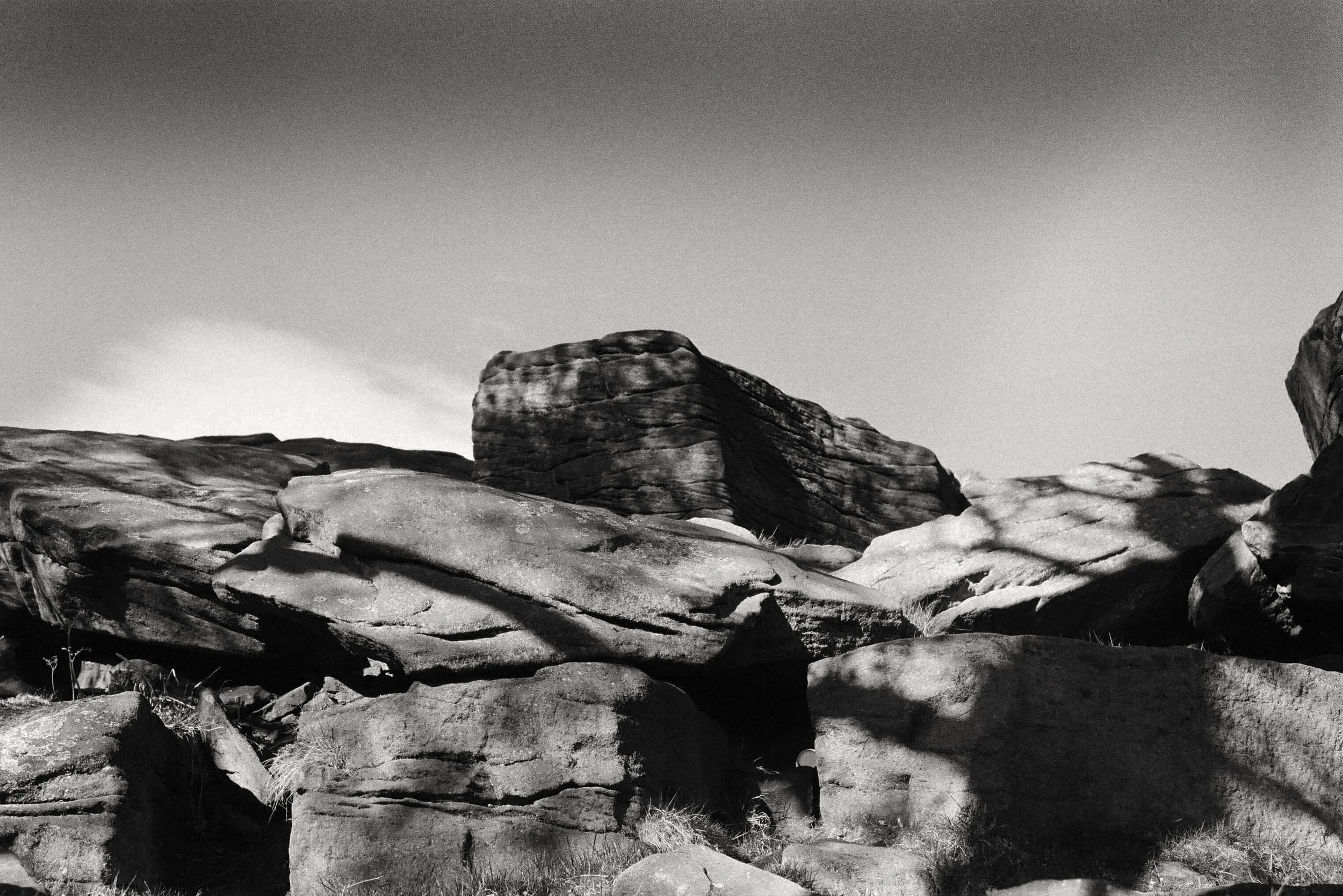 Black and white photographic image of a bare rockscape on a sunny day with heavy shadows and areas of light amidst the uneven shapes