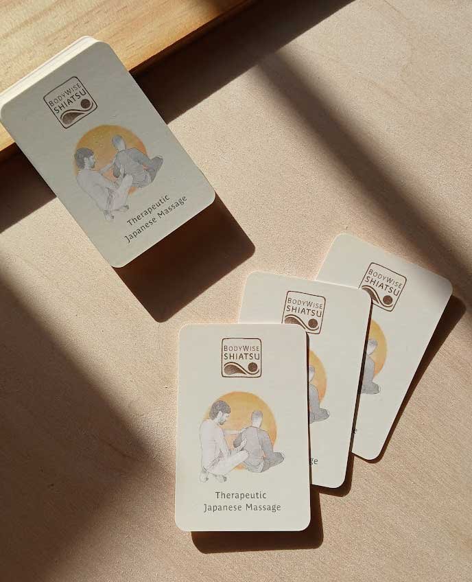 Stack of Bodywise Shiatsu business cards on a sunny wooden surface with shadows