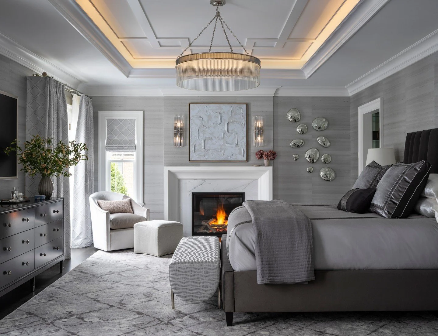 A master suite designed for both elegance and ease ✨
Layers of soft grays, tailored textures, and a glowing fireplace create a space that feels refined yet endlessly inviting. Every detail, from the coffered ceiling to the custom accents, was chosen 