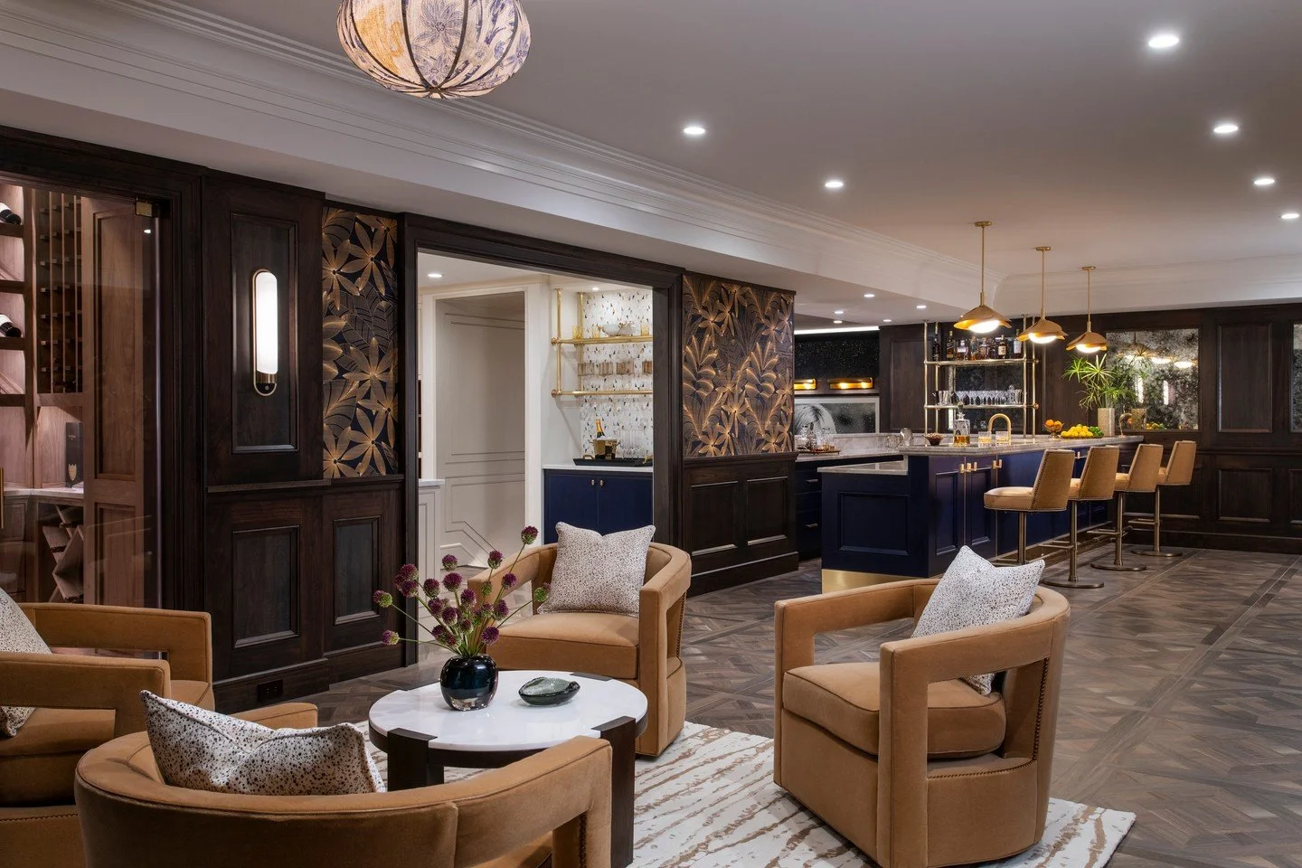 Onto the lower level of this home &mdash; a space inspired by the glamour and intrigue of a New York City speakeasy.
Dark wood paneling, brass details, and deep navy cabinetry create a moody warmth, while custom carved panels and rich textures elevat