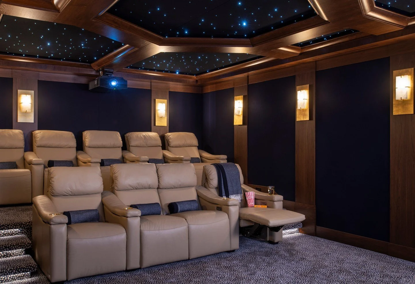 Last but certainly not least in this incredible lower level &mdash; the home movie theater.
Designed with layered lighting, rich navy walls, and a custom wood-paneled ceiling dotted with a starlit glow, this space delivers all the drama of the big sc