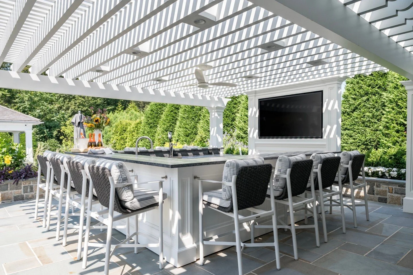 Under the pergola 🤍
This custom bar was designed as the ultimate gathering spot &mdash; shaded by crisp white beams that cast the most beautiful light and shadow throughout the day. Woven bar stools, tailored cushions, and natural stone create a loo
