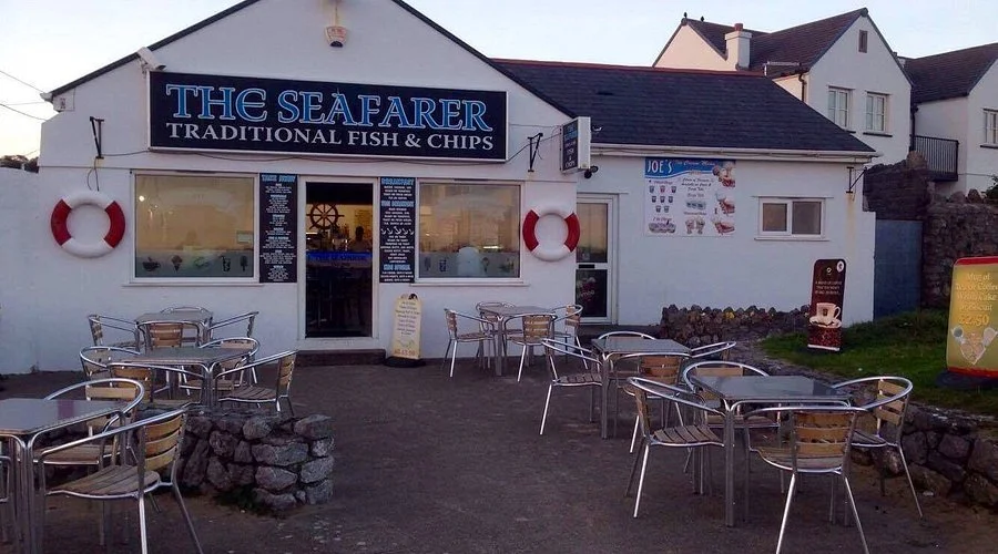 A fish and chips restaurant named "The Seafarer" with outdoor seating, displaying nautical decor with lifebuoys on the wall.