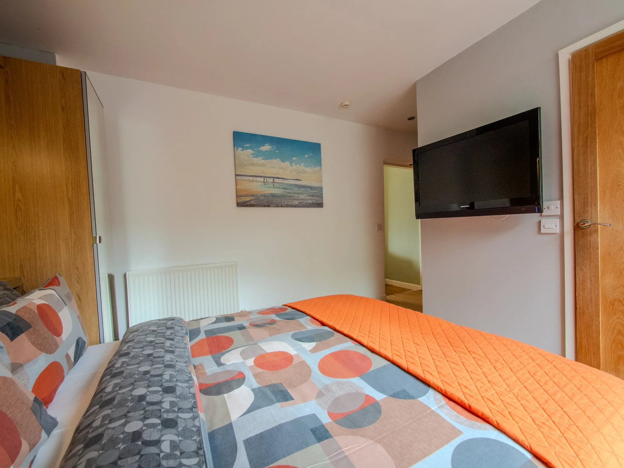 A bedroom with two beds, colorful polka dot bedding, a wall-mounted flat-screen TV, a framed beach scene picture, and wooden furniture.