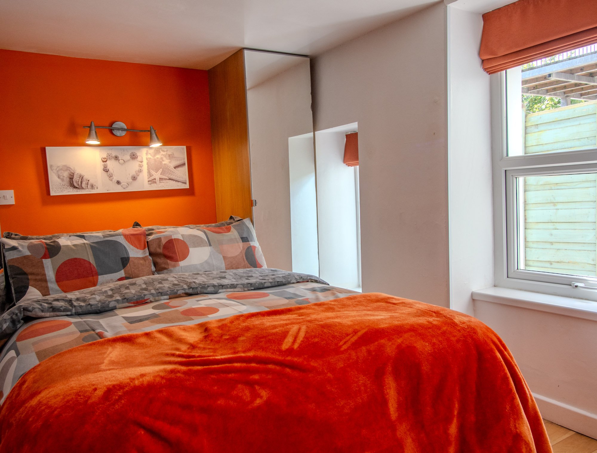 A bedroom with an orange accent wall, making the bed with patterned and solid orange blankets.