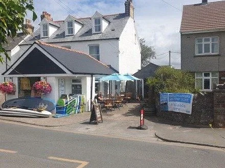 Cafe with outdoor seating, surfboards on display, and street view.