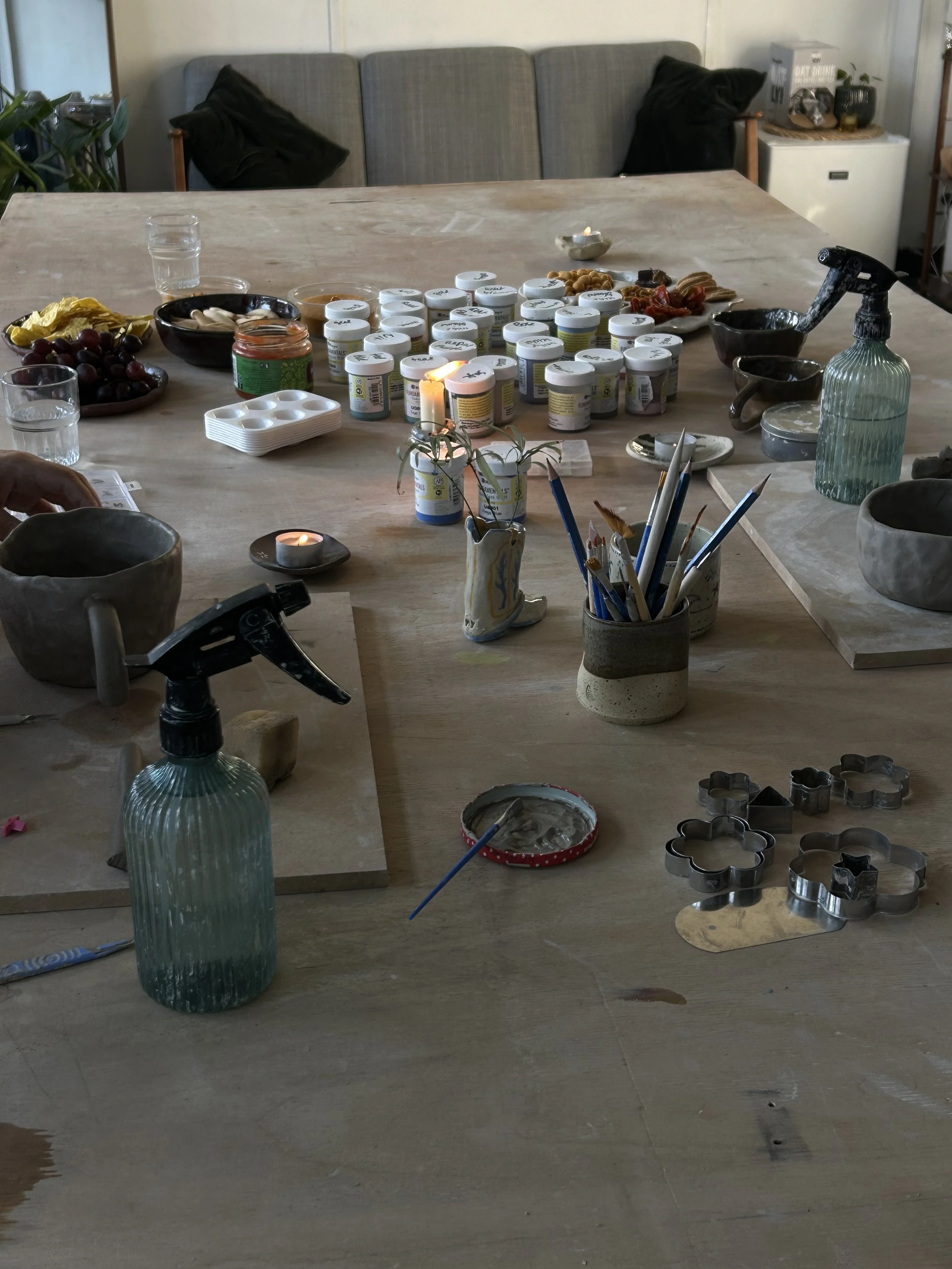 Een tafel met verschillende potjes verf, schildergereedschap, bakjes en decoratieve spullen, klaar voor een creatieve activiteit.