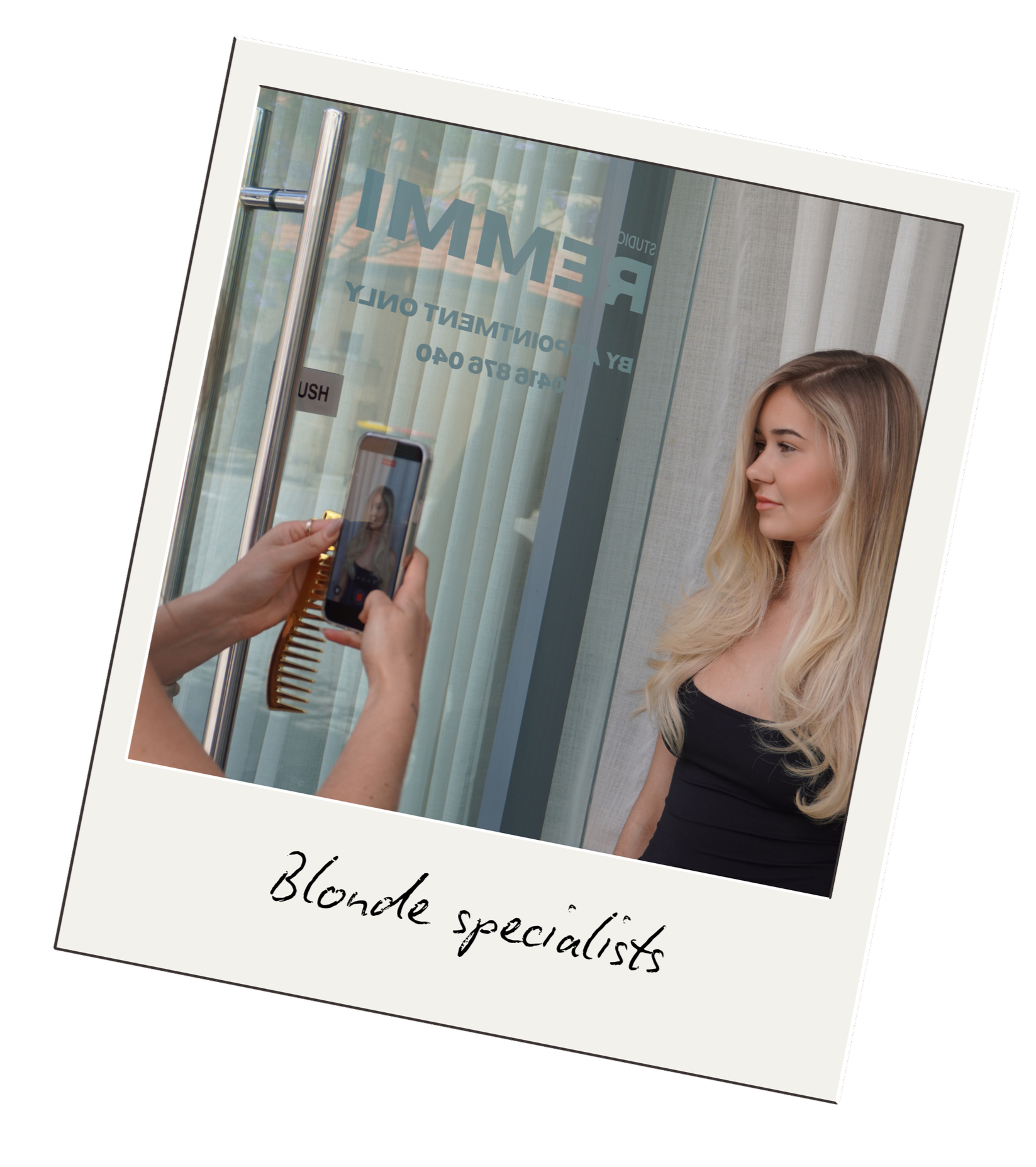 Blonde woman having her hair photographed by a person using a smartphone, in a salon with glass doors and curtains.