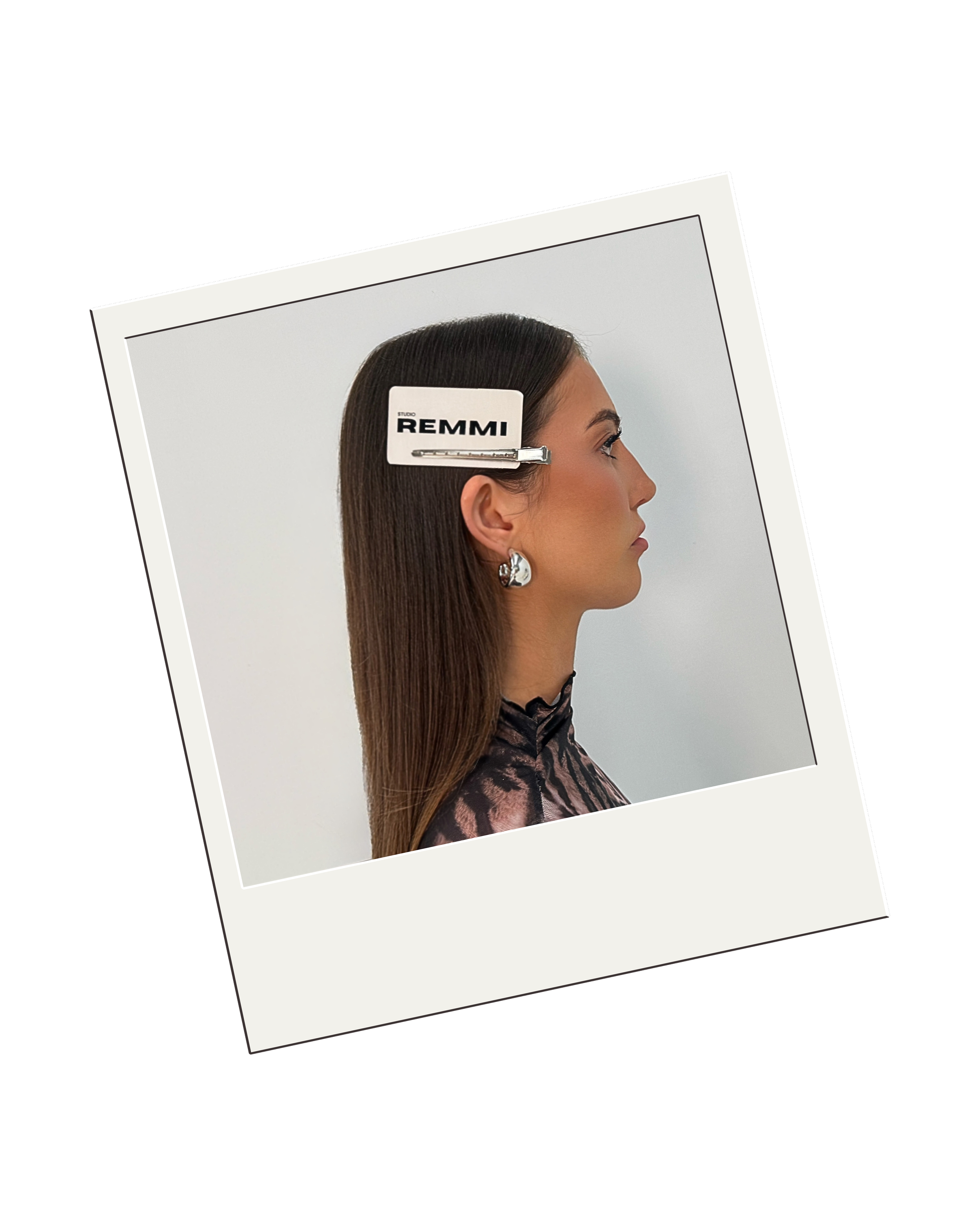 Side profile of a woman with long straight brown hair, wearing earrings and a patterned top, with a hair clip labeled 'REMMI' on her head.