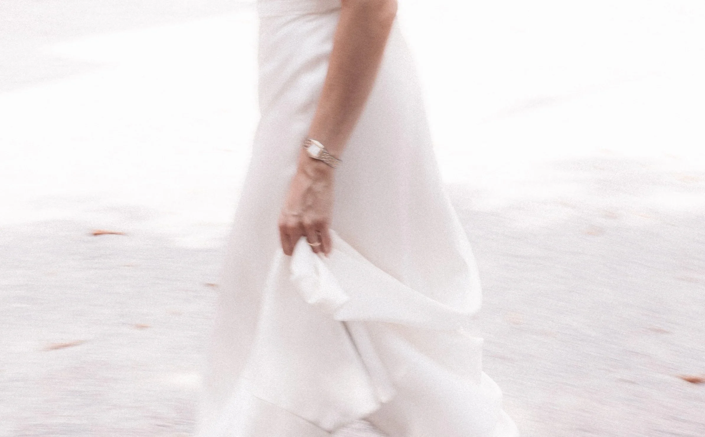Nahaufnahme eines weißen Kleides auf einem Hintergrund, die Hand einer Person, die das Kleid hält, trägt eine große Uhr.