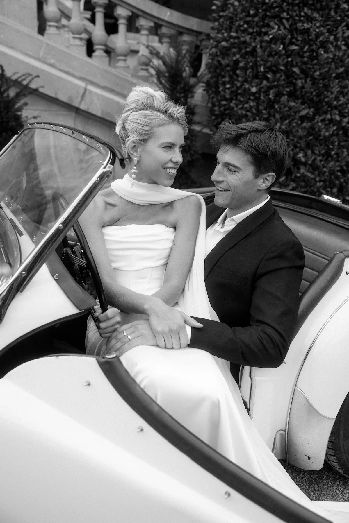 Ein glückliches Brautpaar sitzt in einem Oldtimer-Cabriolet, das vermutlich für eine Hochzeit genutzt wird.