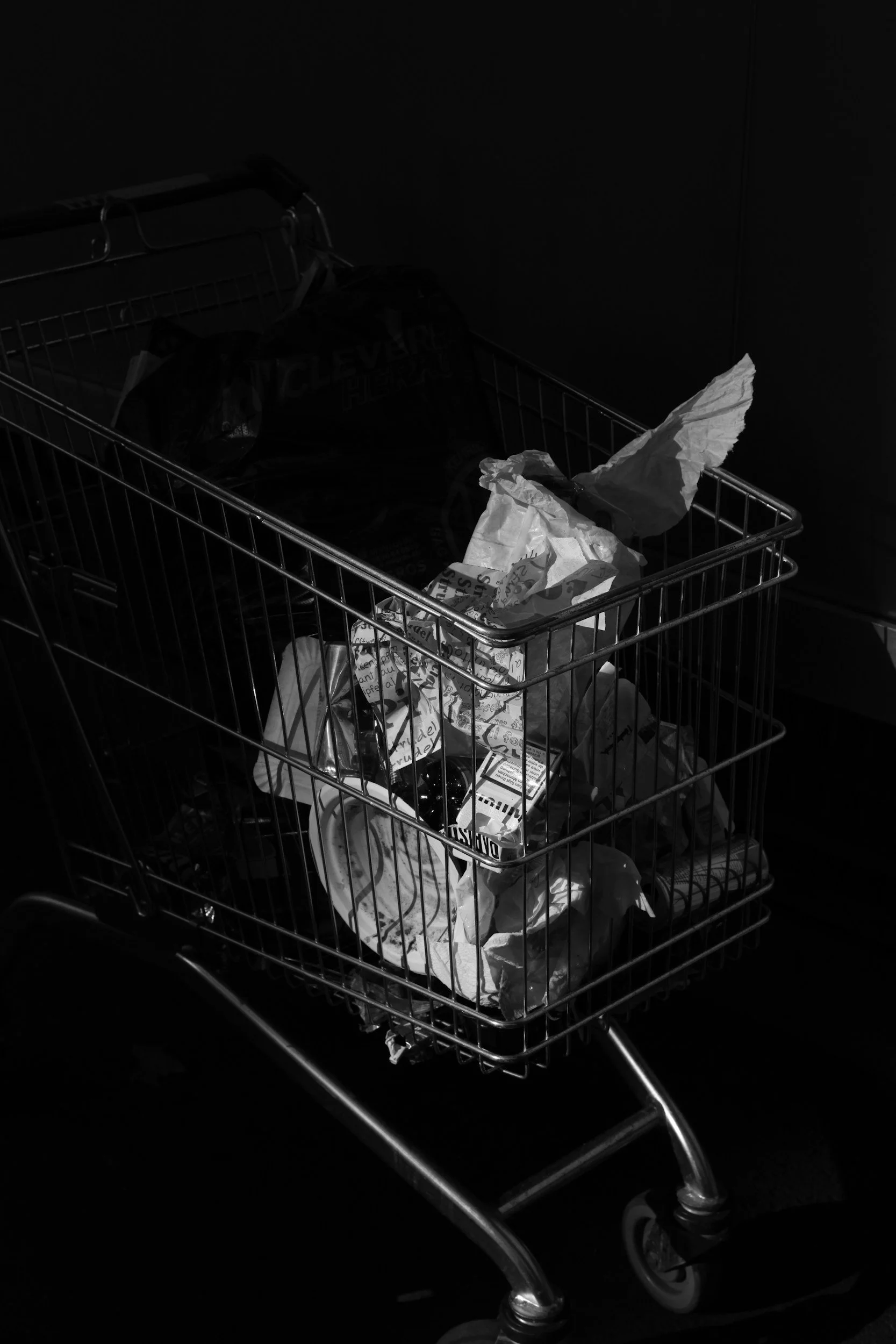 Empty shopping cart with crumpled paper bags inside, in a dark environment.