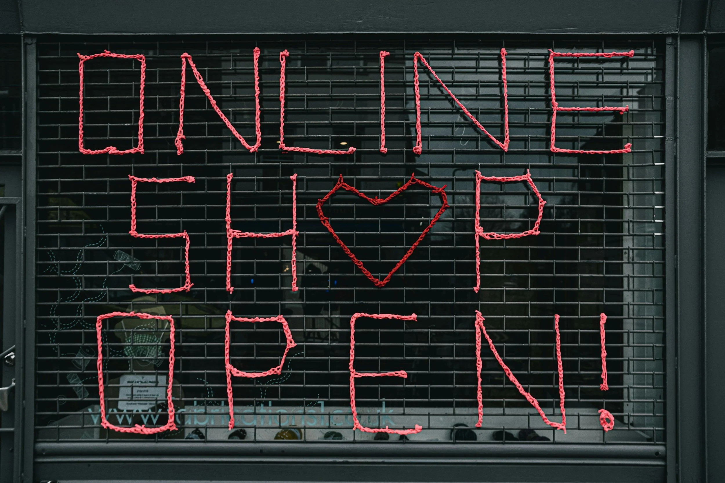 A neon sign in red reading 'ONLINE SHOP' on a black metal grid background.