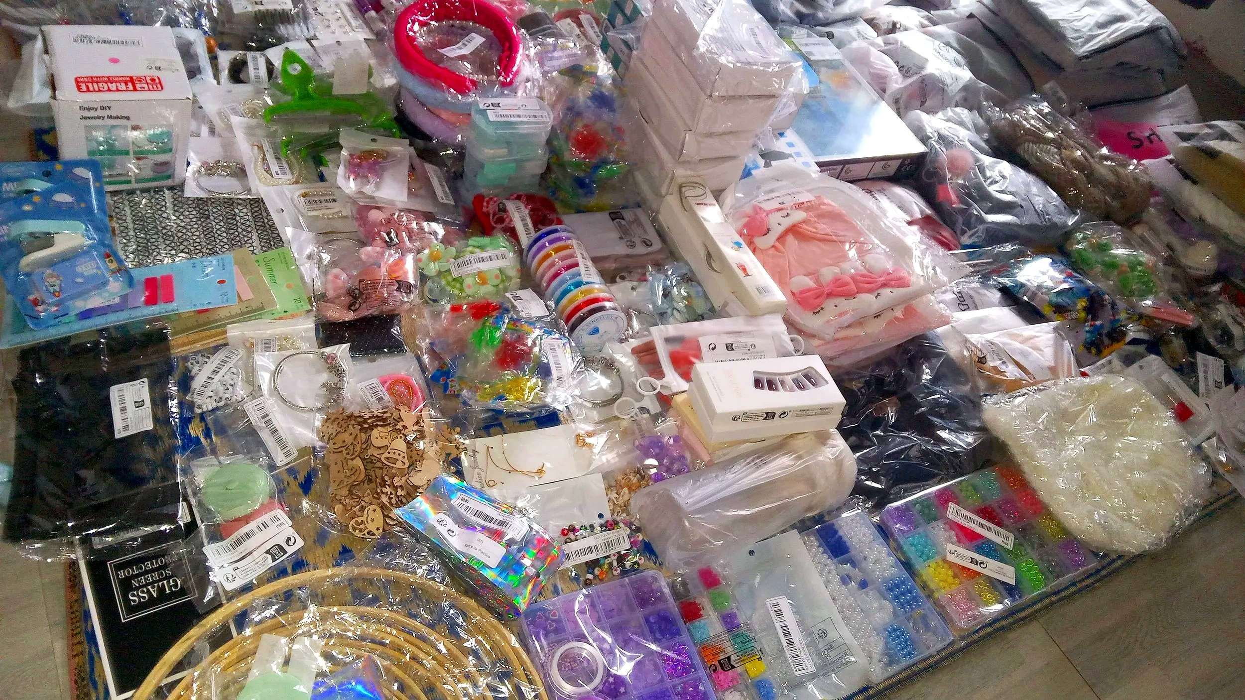 A large assortment of colorful craft supplies and jewelry making materials, including beads, ribbons, charms, and decorative items, spread out on a table.