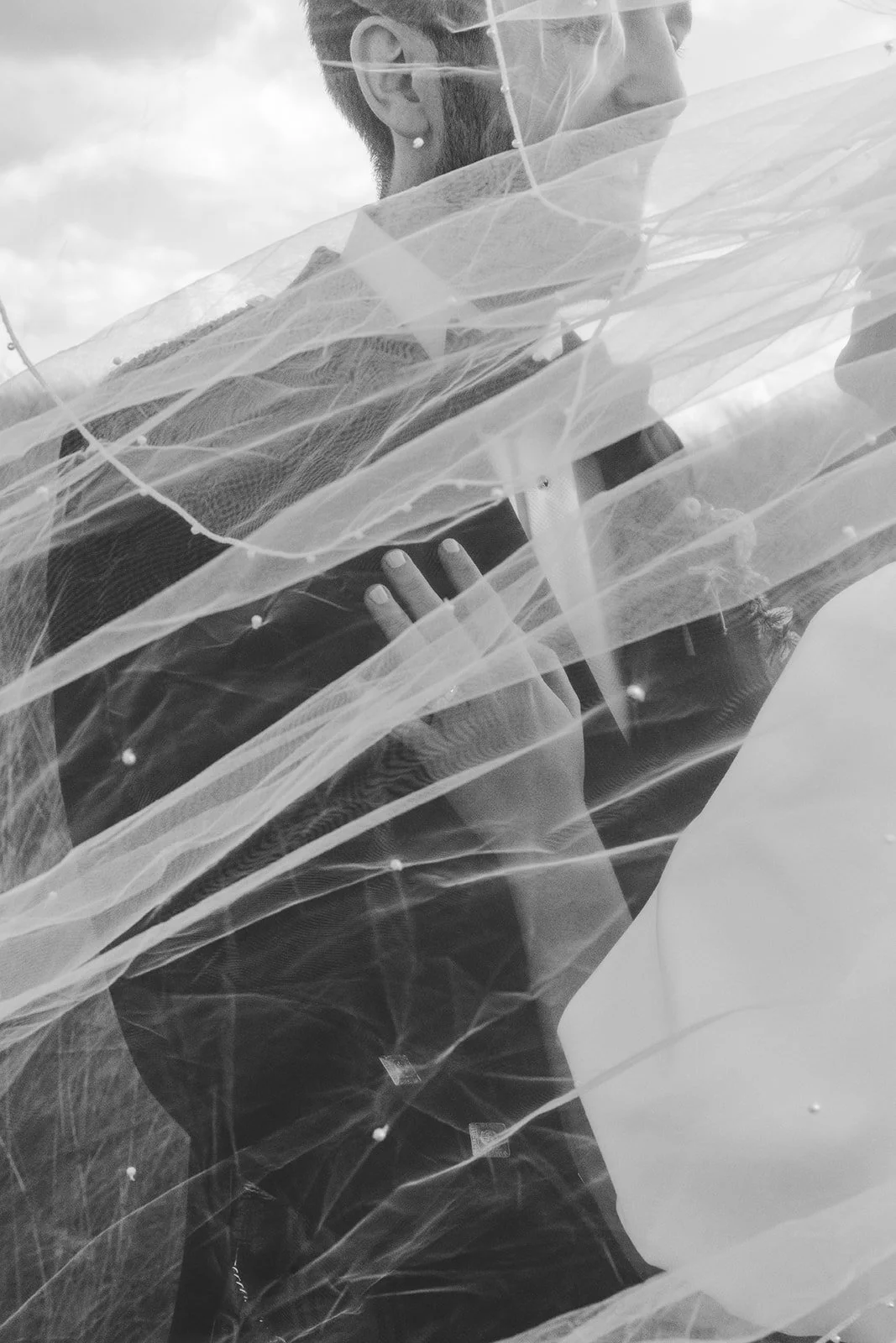 A woman with face partially covered by a veil, looking to the side, outdoors with cloudy sky in background.