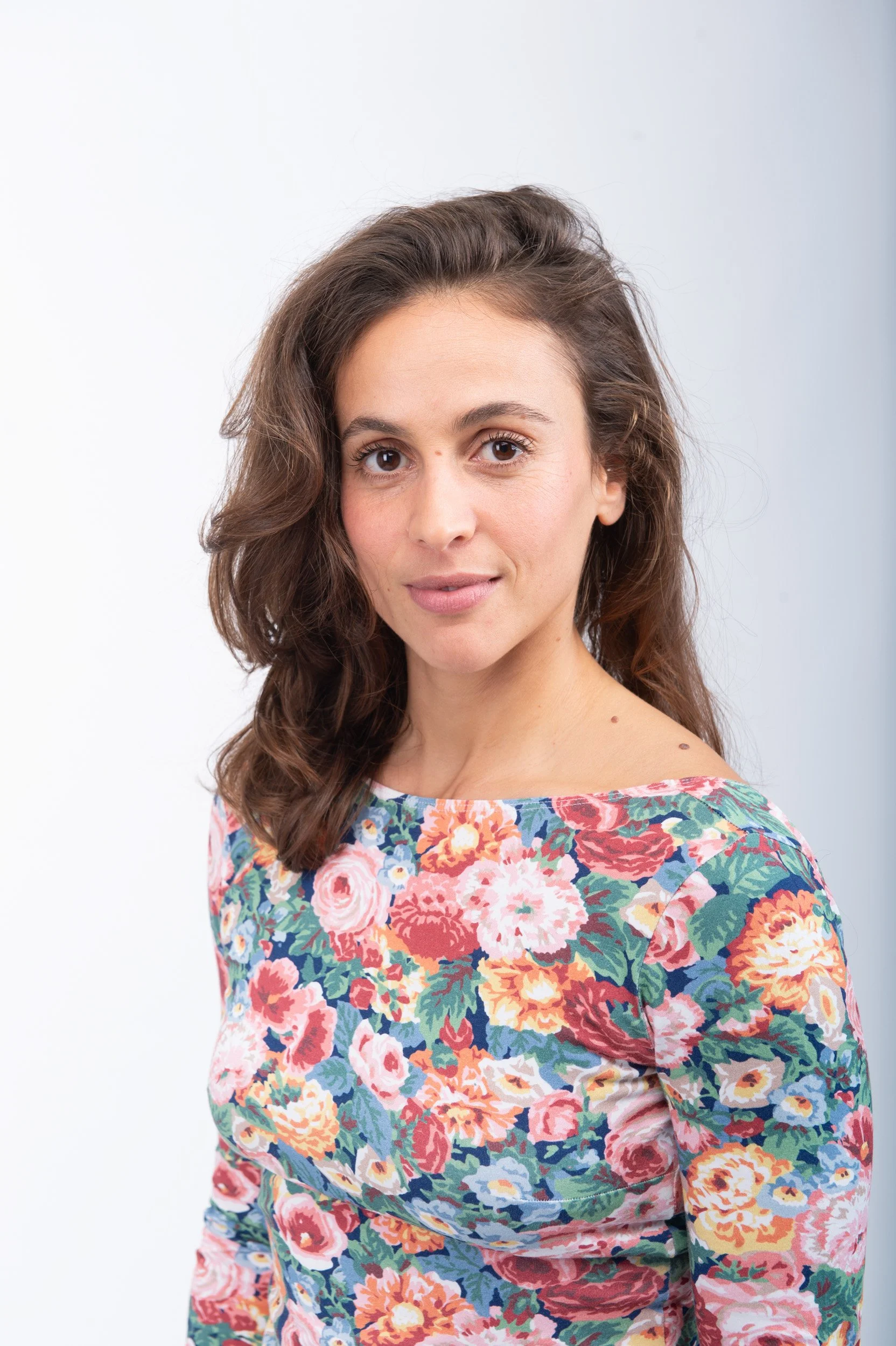 Jeune femme aux cheveux bruns et à la peau claire, portant un haut à motif floral multicolore, regardant l'objectif.