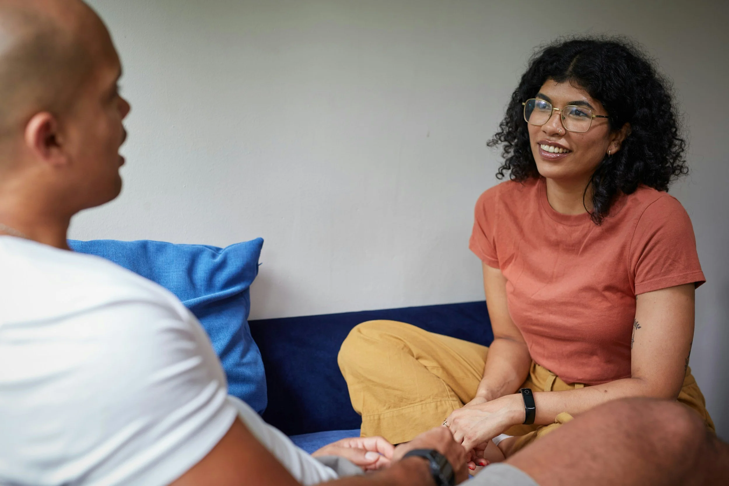 A woman with curly black hair and glasses smiling while talking with a man who is sitting next to her.