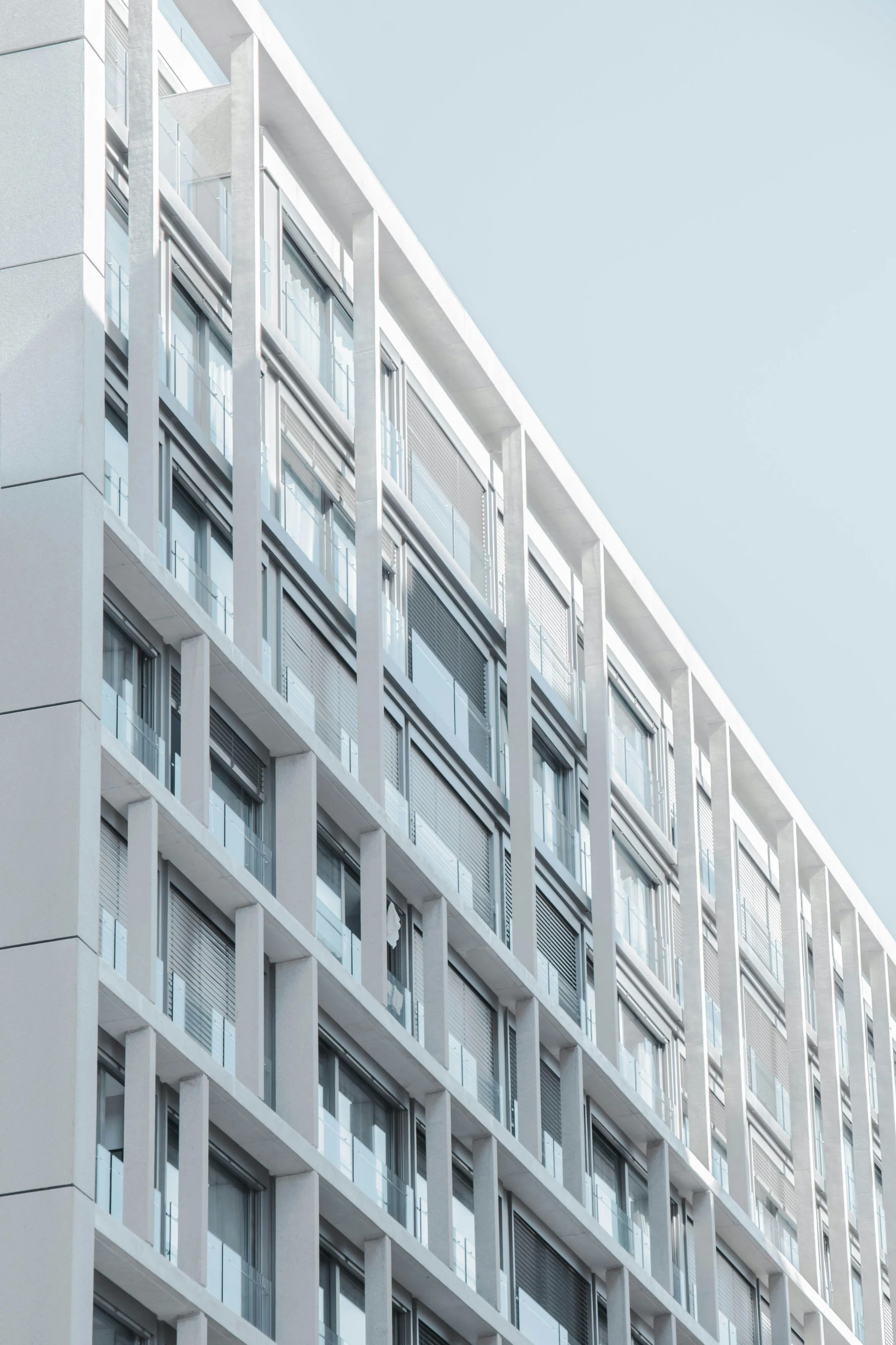 Modern multi-story apartment building with glass balconies and windows, under a clear blue sky.