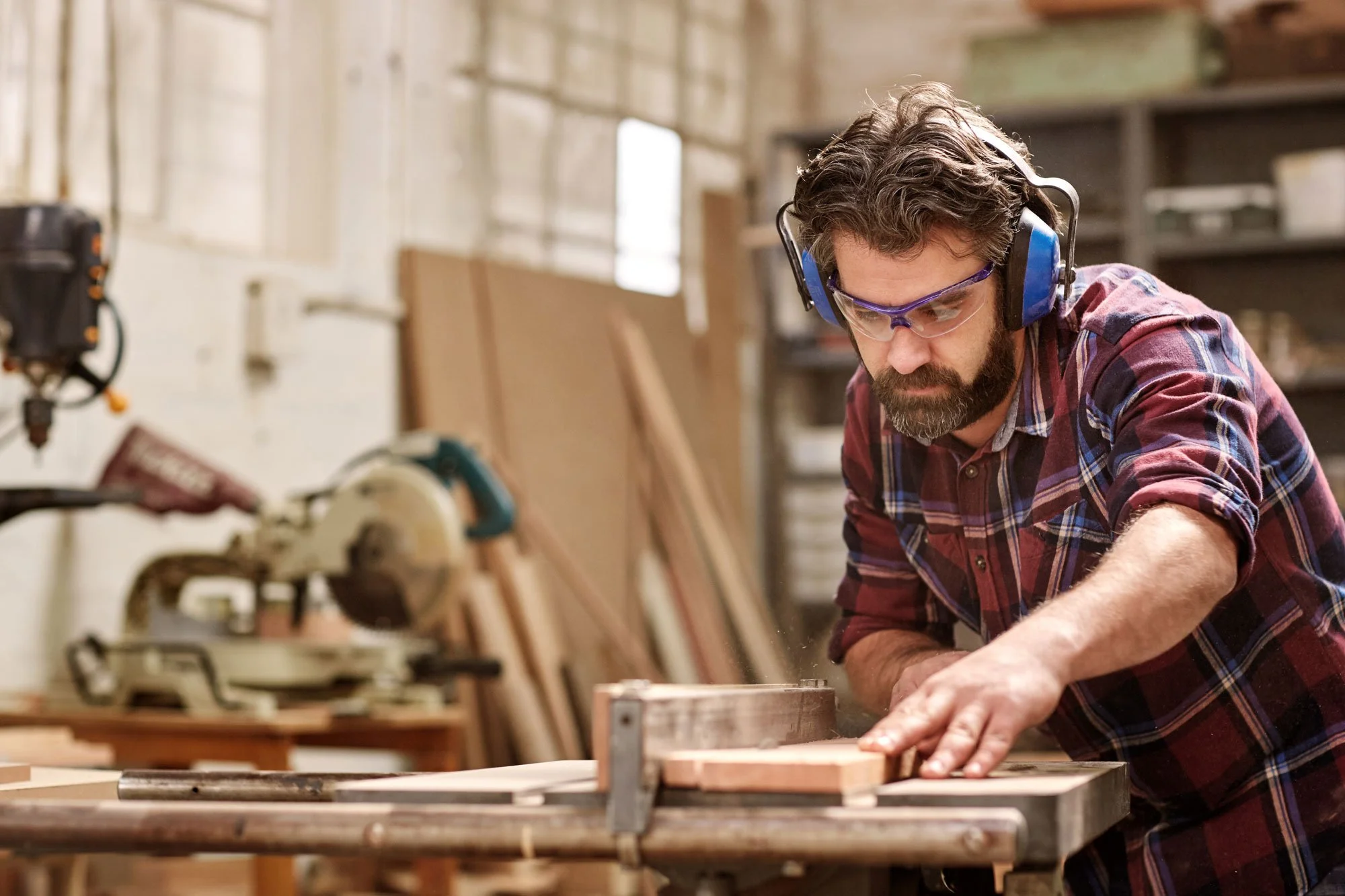 A man wearing safety glasses and ear protection working on a woodworking project in a workshop.