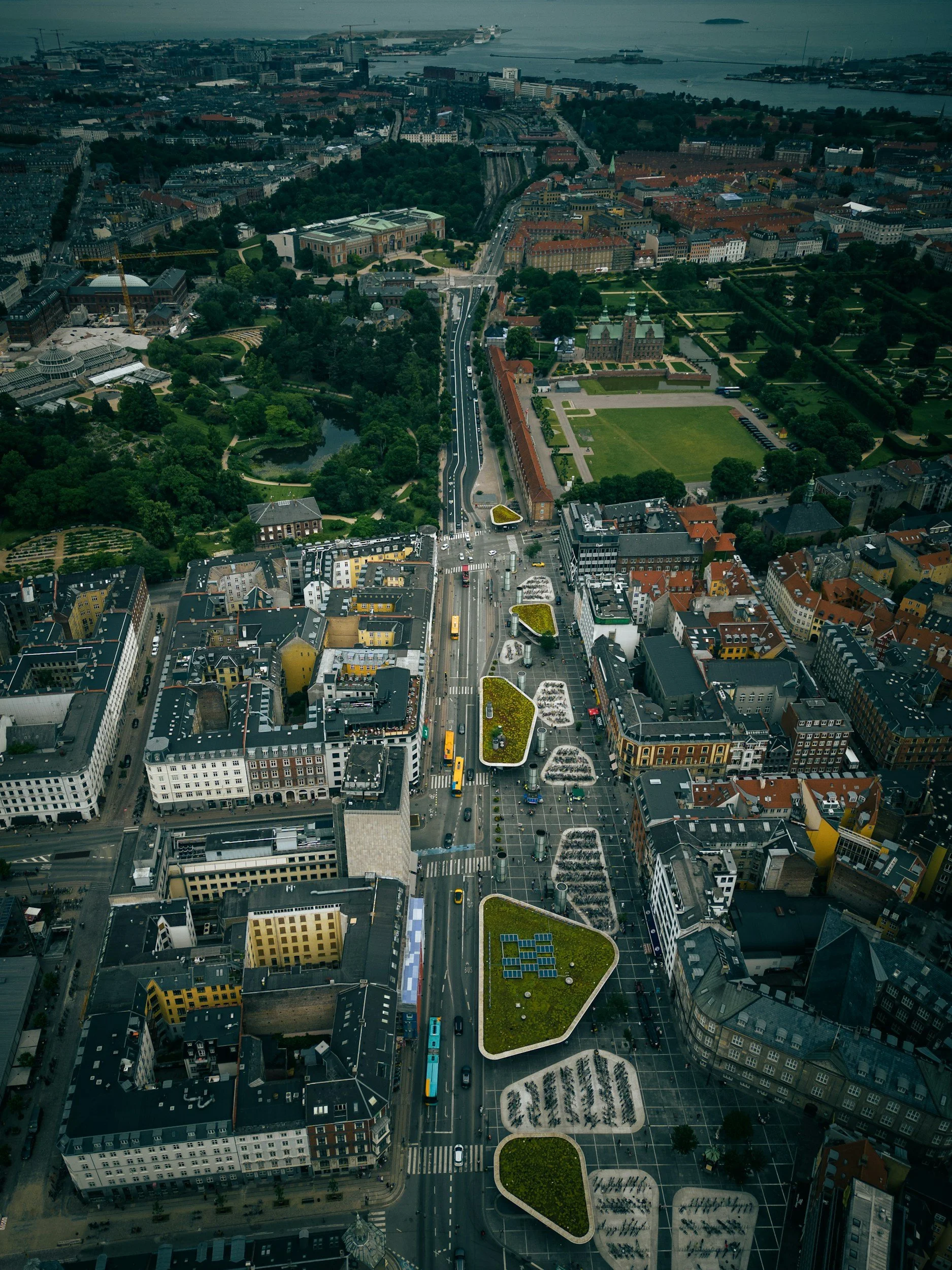 Aerial view of a cityscape with green parks, roads, and buildings in a downtown area, extending to a waterfront.