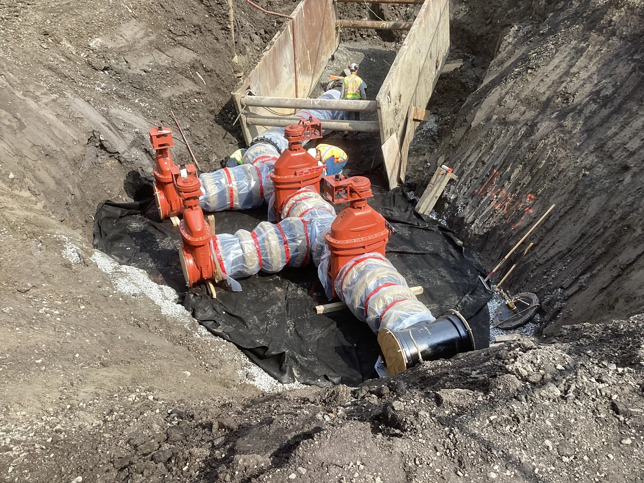 Travailleurs en train d'installer un système de tuyauterie dans une fosse lors de travaux de construction ou de réparation de pipeline.