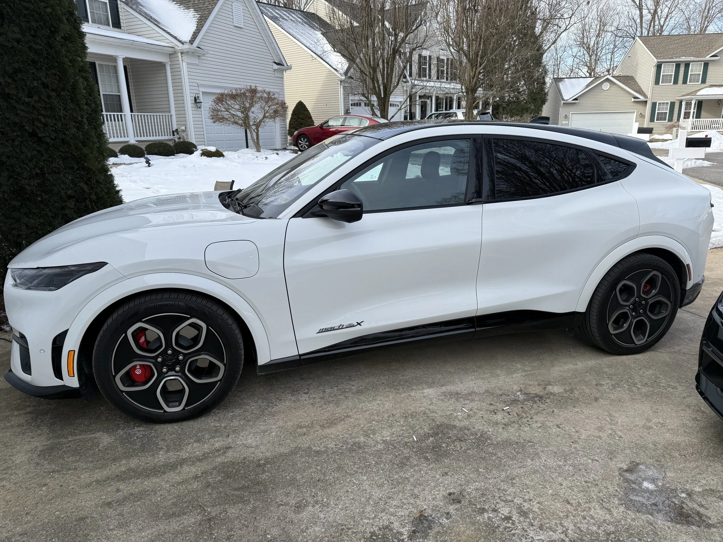 White electric car parked in a residential driveway, with black accents and red brake calipers, during winter.