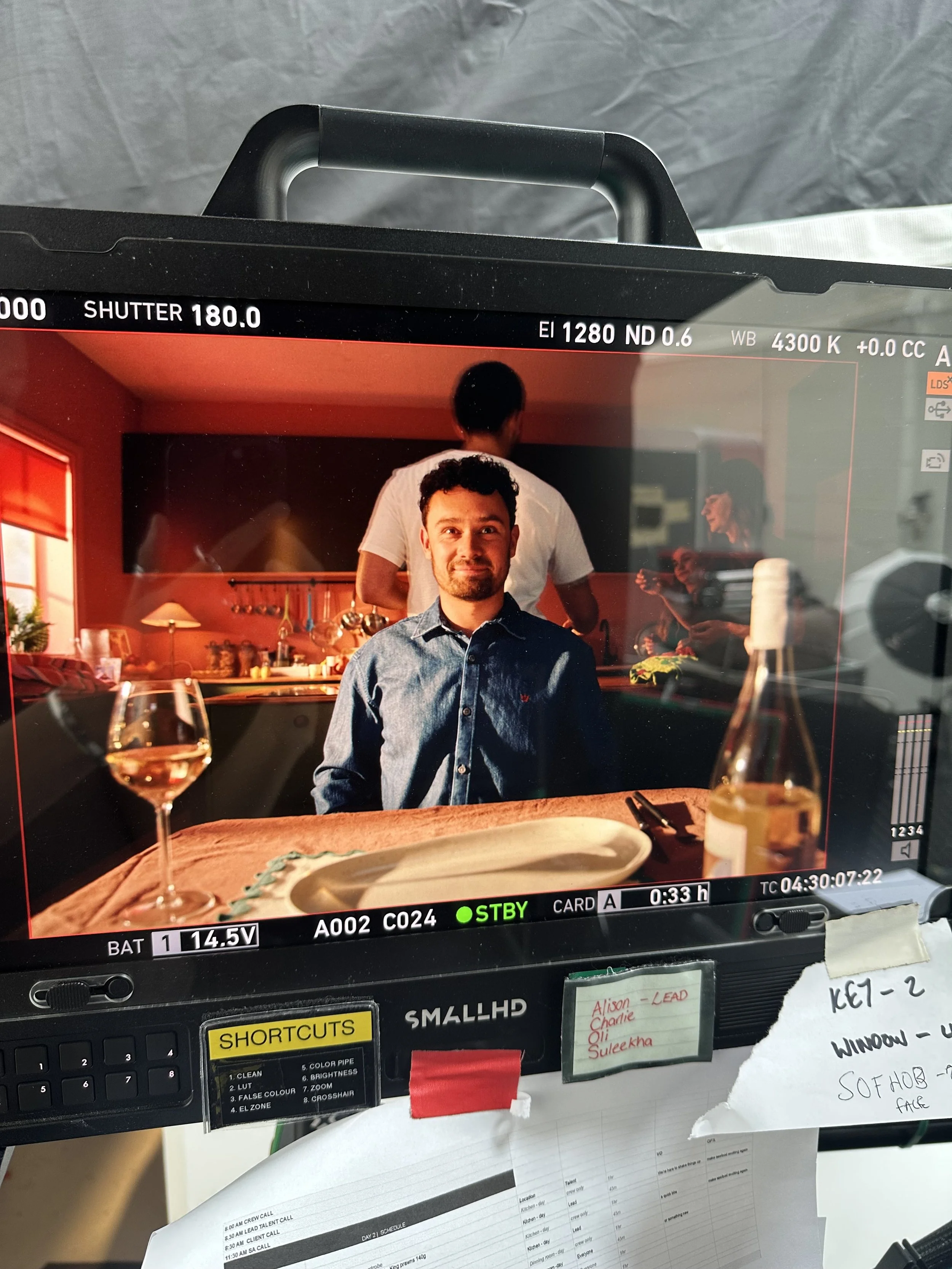 videocamera screen mid filming real seafood co brand film with man at table with glass of wine in green and red kitchen in dramatic lighting