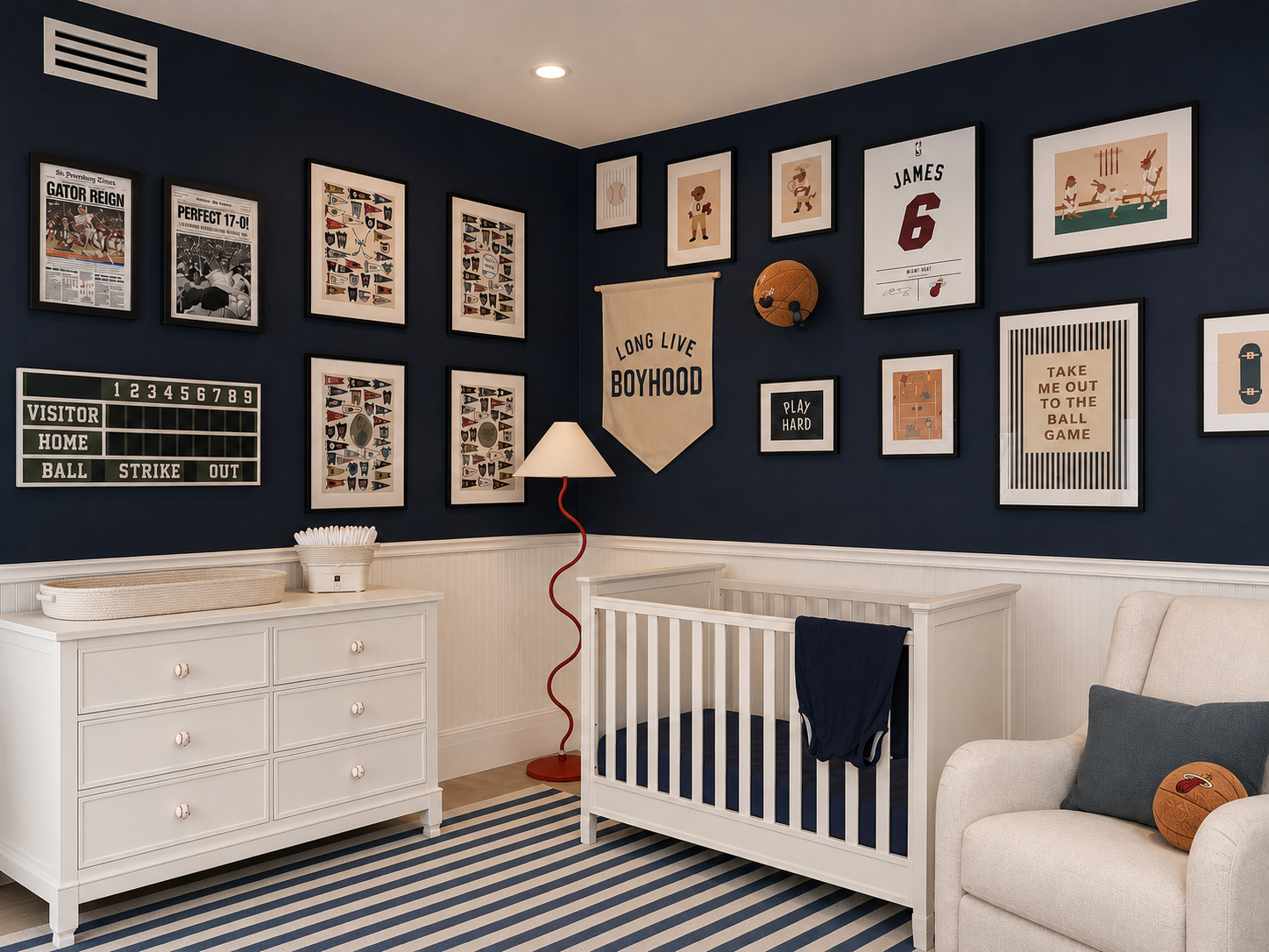 Nursery room with sports-themed decor, white dresser, changing table, crib, armchair, and multiple framed sports posters and artwork on navy blue walls.
