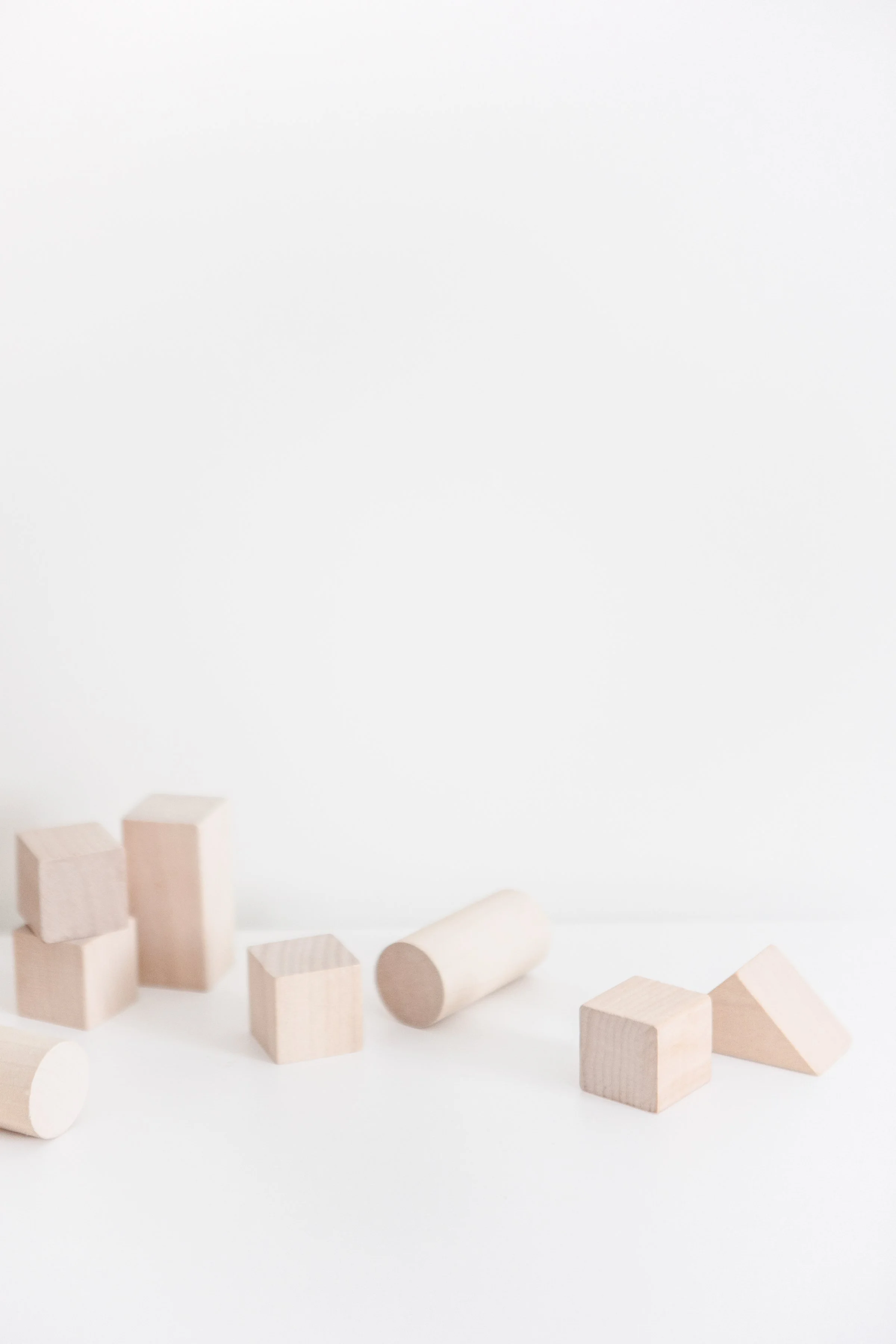 Various light-colored wooden blocks and cylinders scattered on a white surface against a white background.