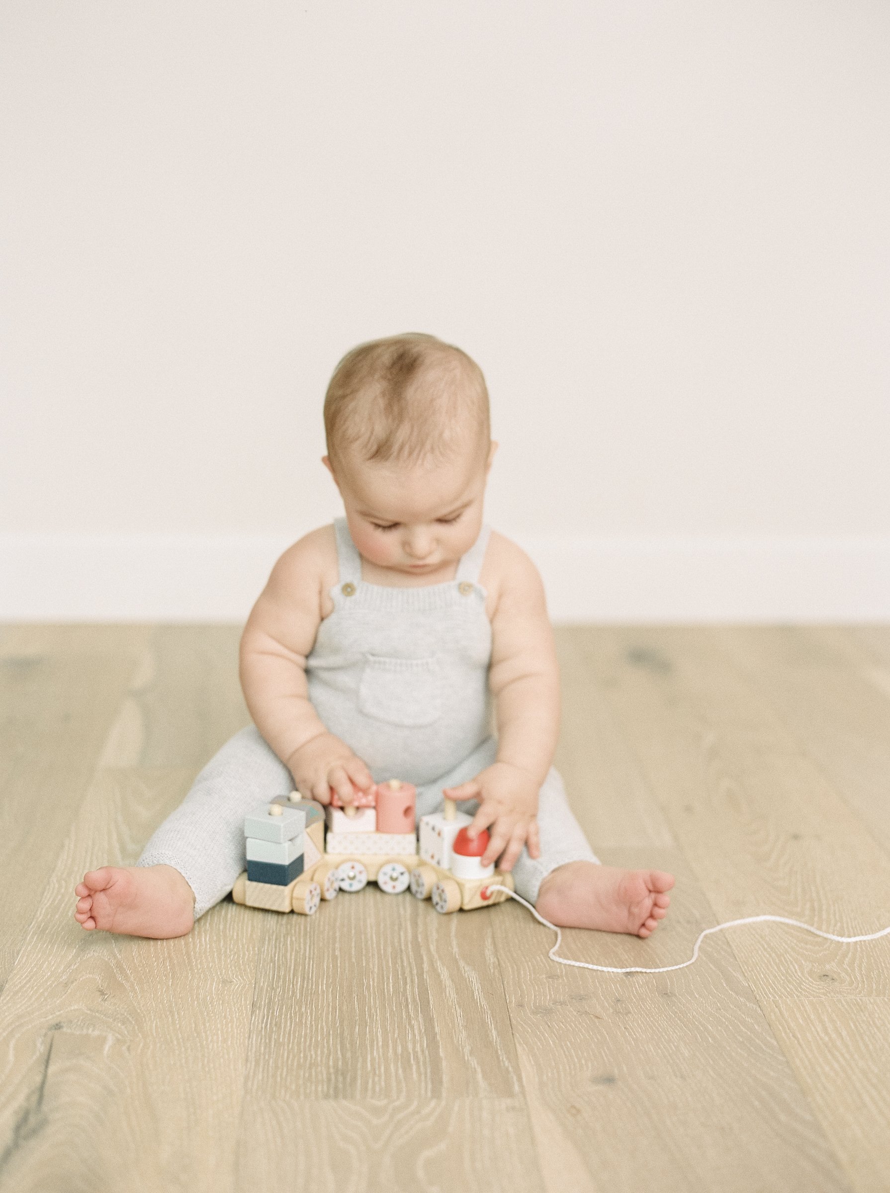 A baby sitting on a wooden floor playing with a wooden toy train.
