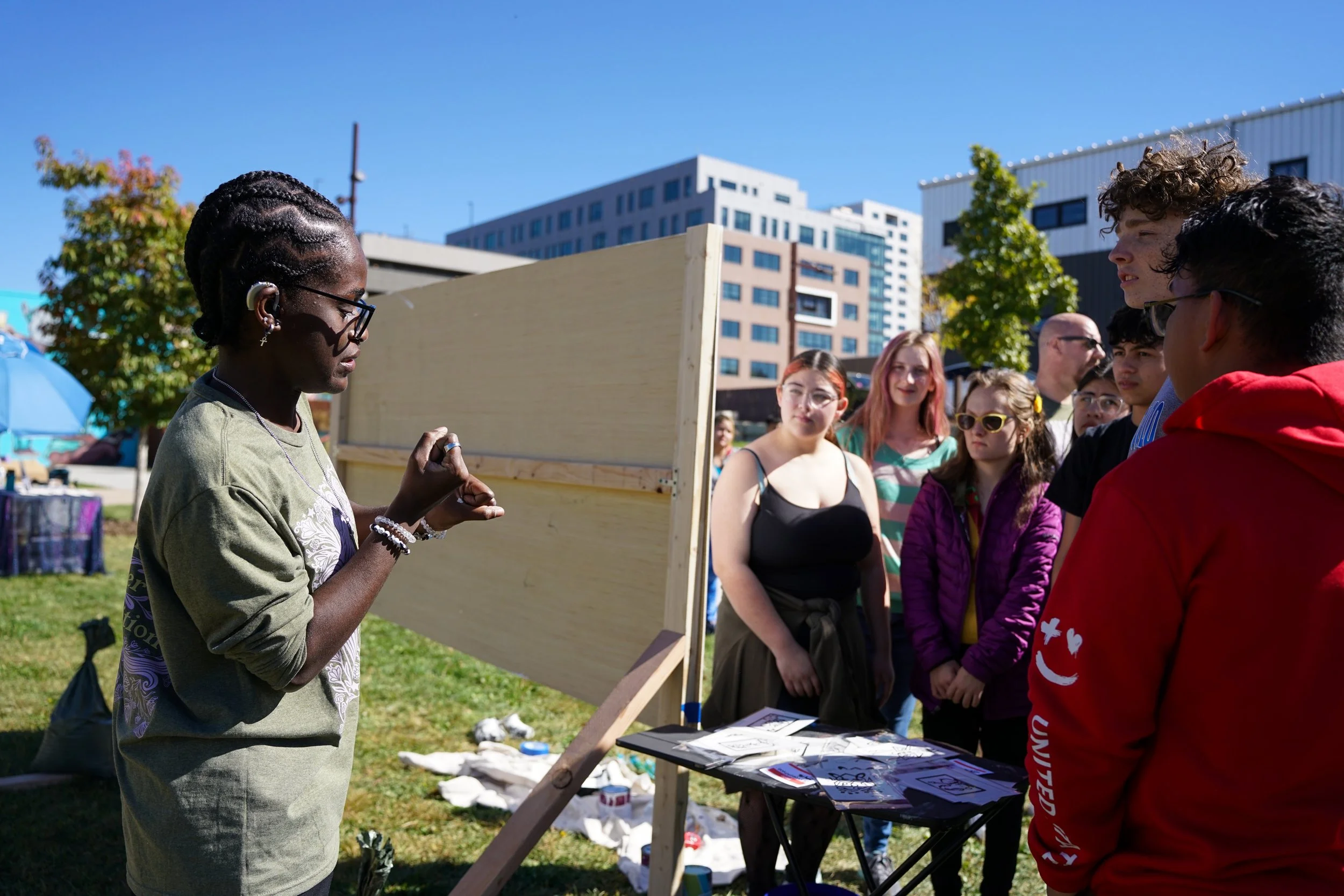 A mural artist faces a crowd of people beside their mural panel