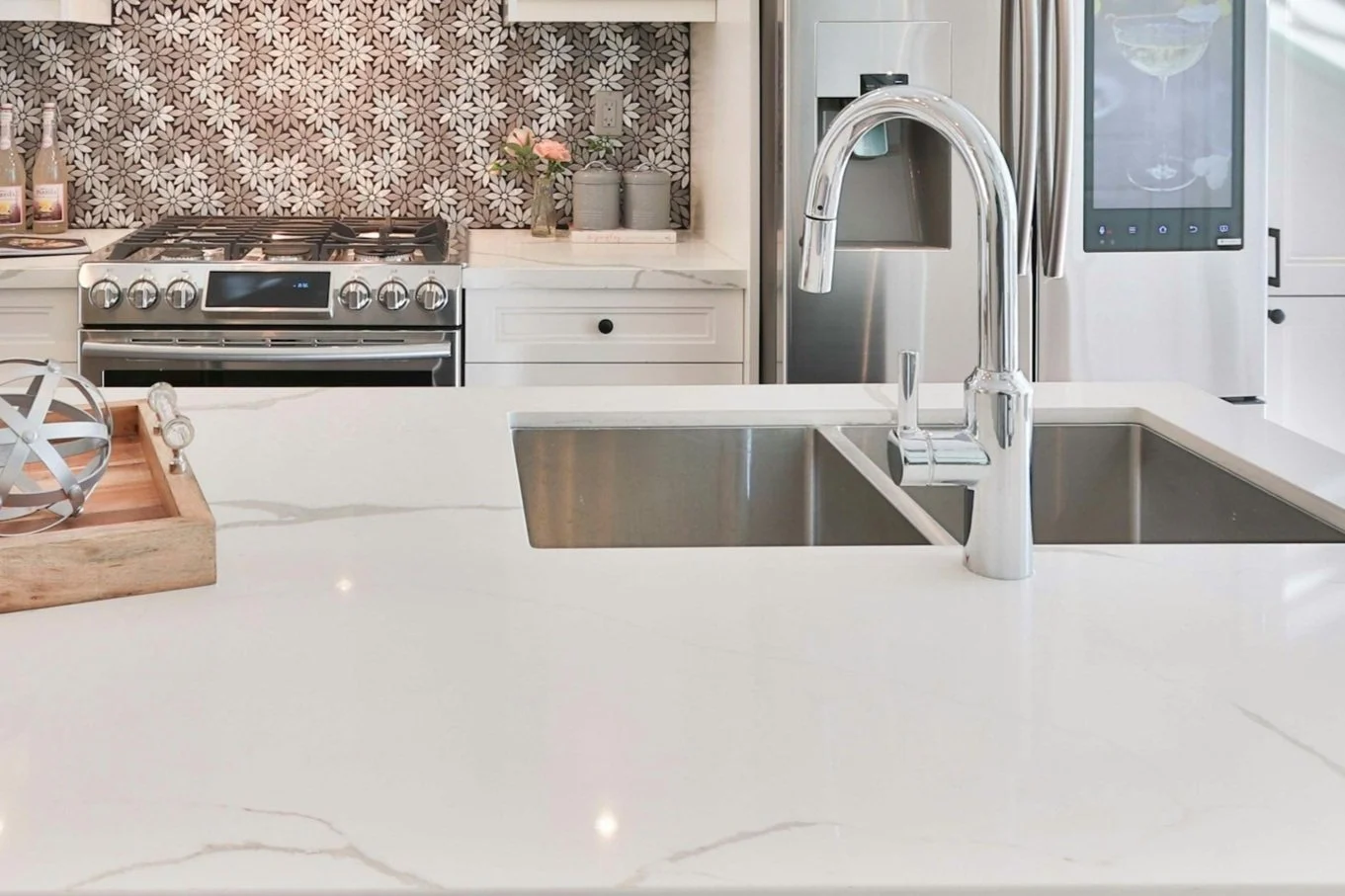 Modern kitchen with white marble countertops, stainless steel sink, and a silver faucet, featuring patterned backsplash, decorative flowers, and stainless steel appliances.