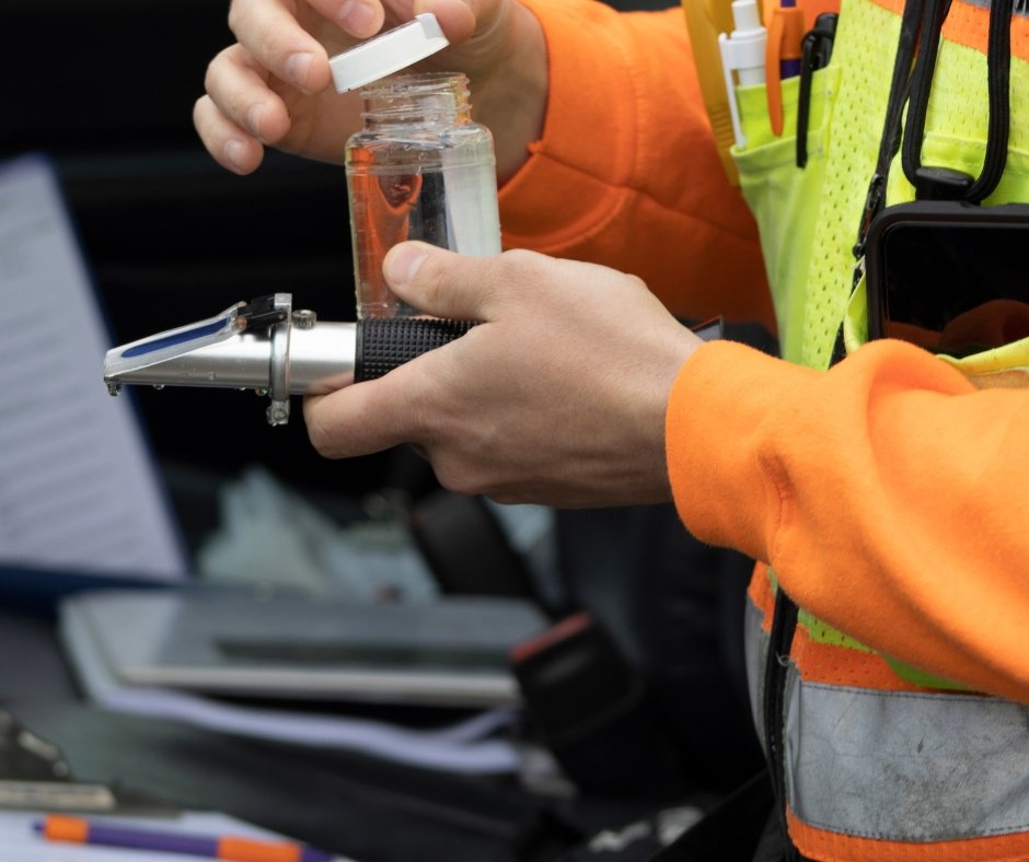 Person wearing a reflective safety vest and orange long-sleeve shirt handling a small jar and a handheld torch.