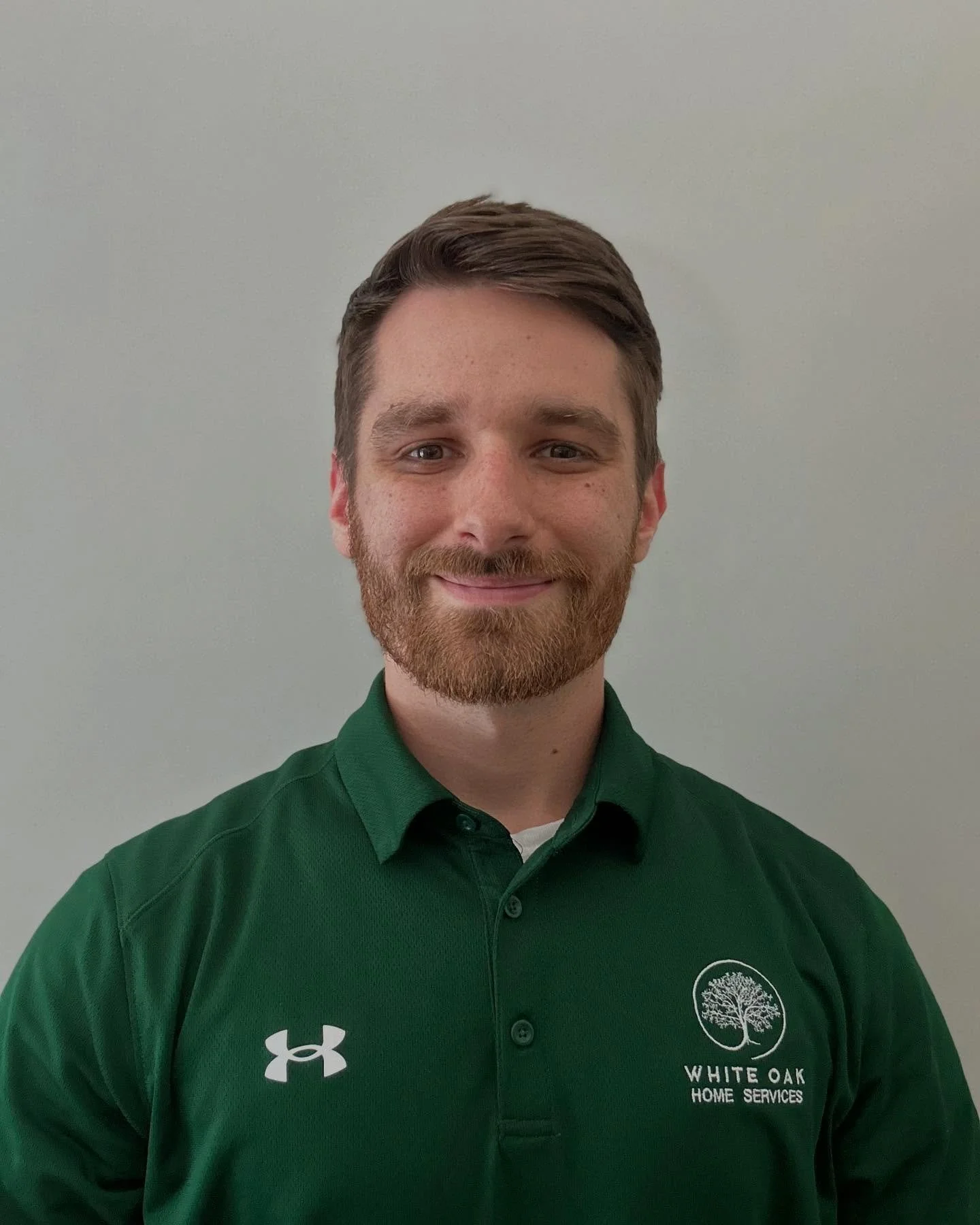 A man with brown hair and a beard smiling, wearing a green polo shirt with the White Oak Home Services logo.