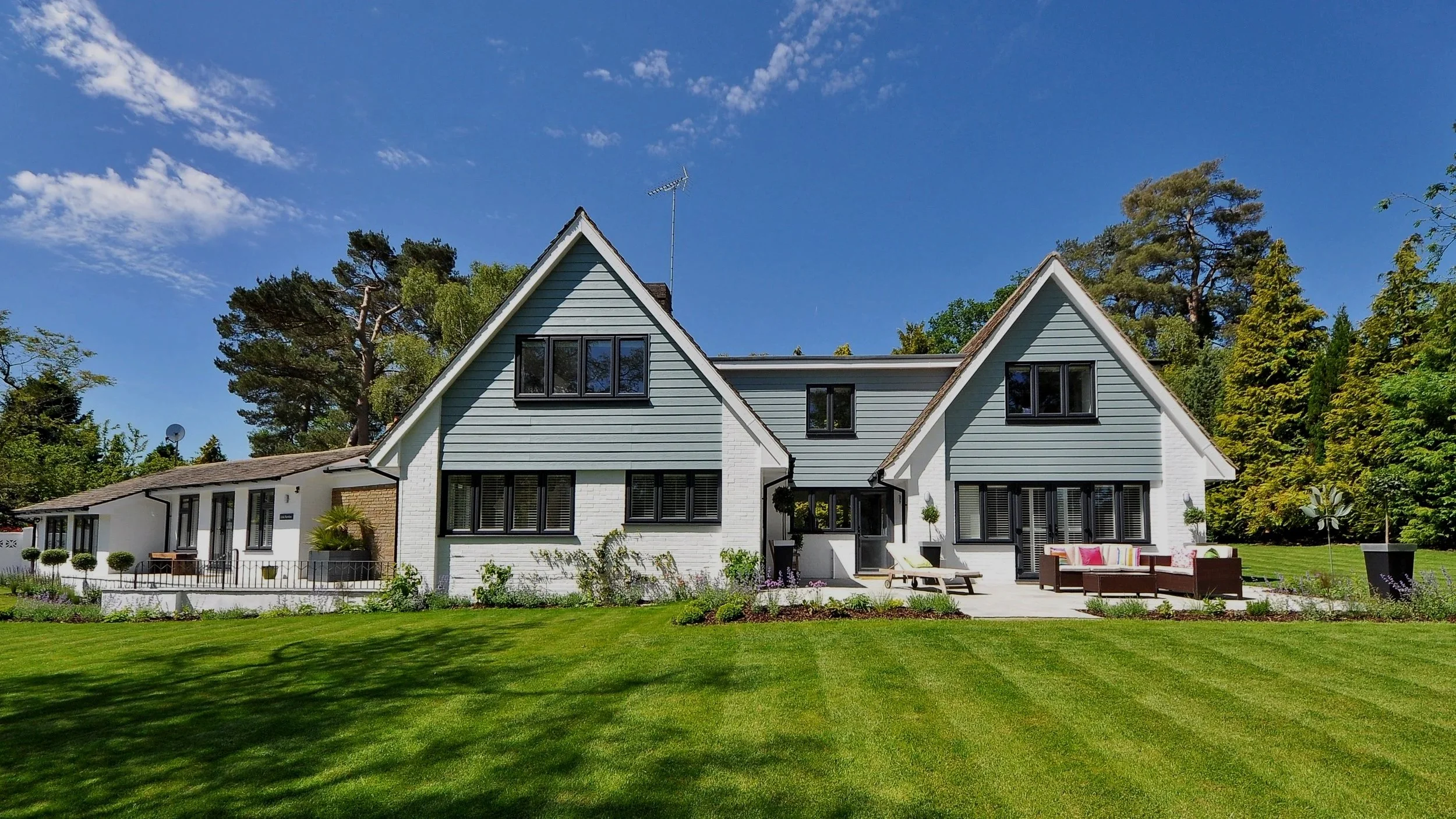 Modern house with green lawn and patio furniture under a blue sky