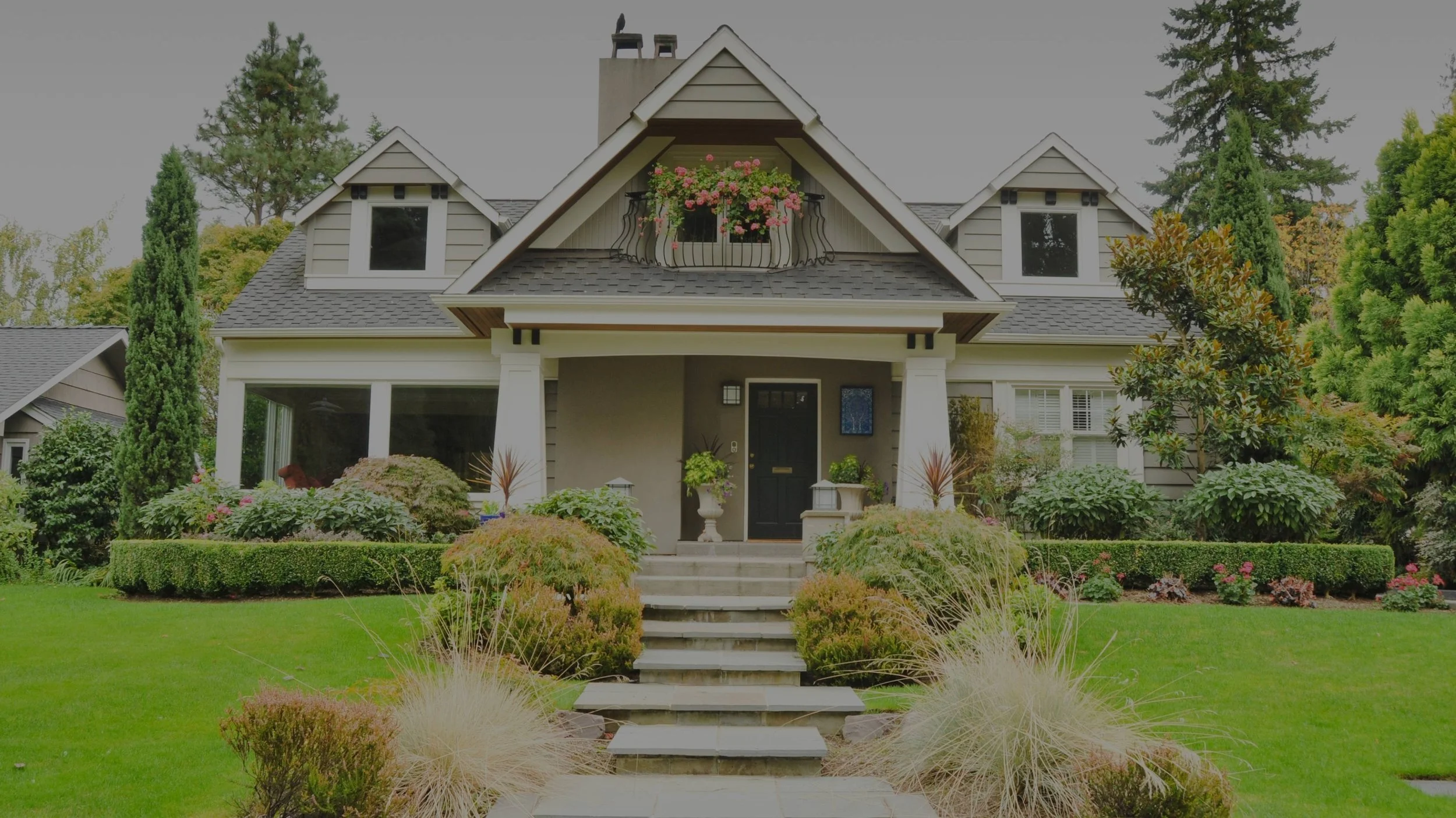 Front view of a two-story house with gray siding, black front door, and landscaped front yard with green grass, shrubs, and trees.