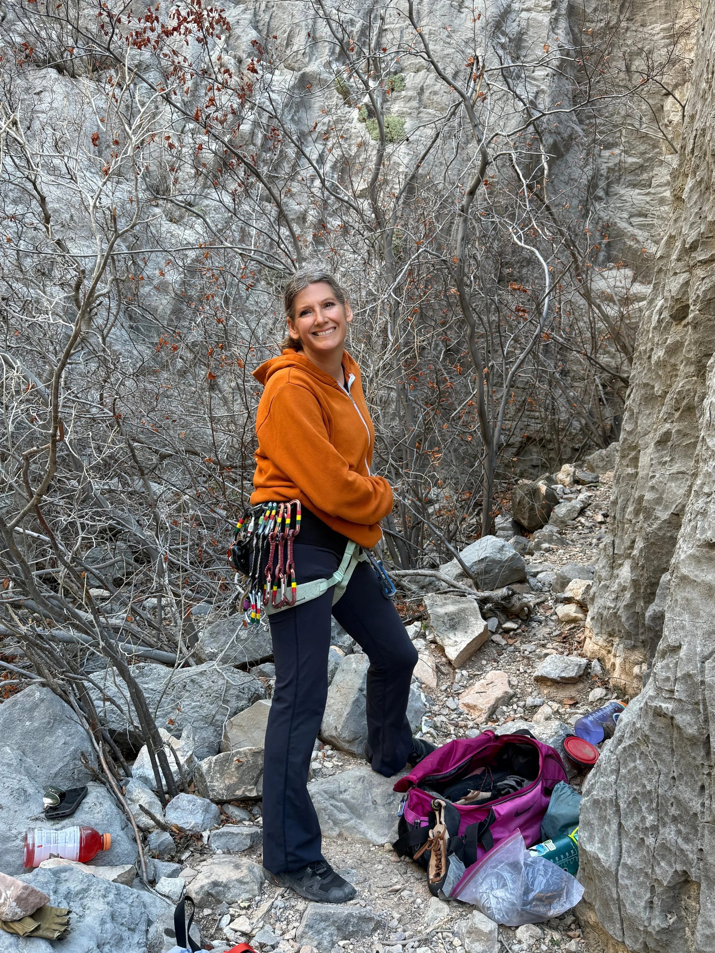A woman standing on a rocky mountain summit, holding a sign that reads "Borah Peak 12,662 ft," with mountain peaks and landscapes in the background.